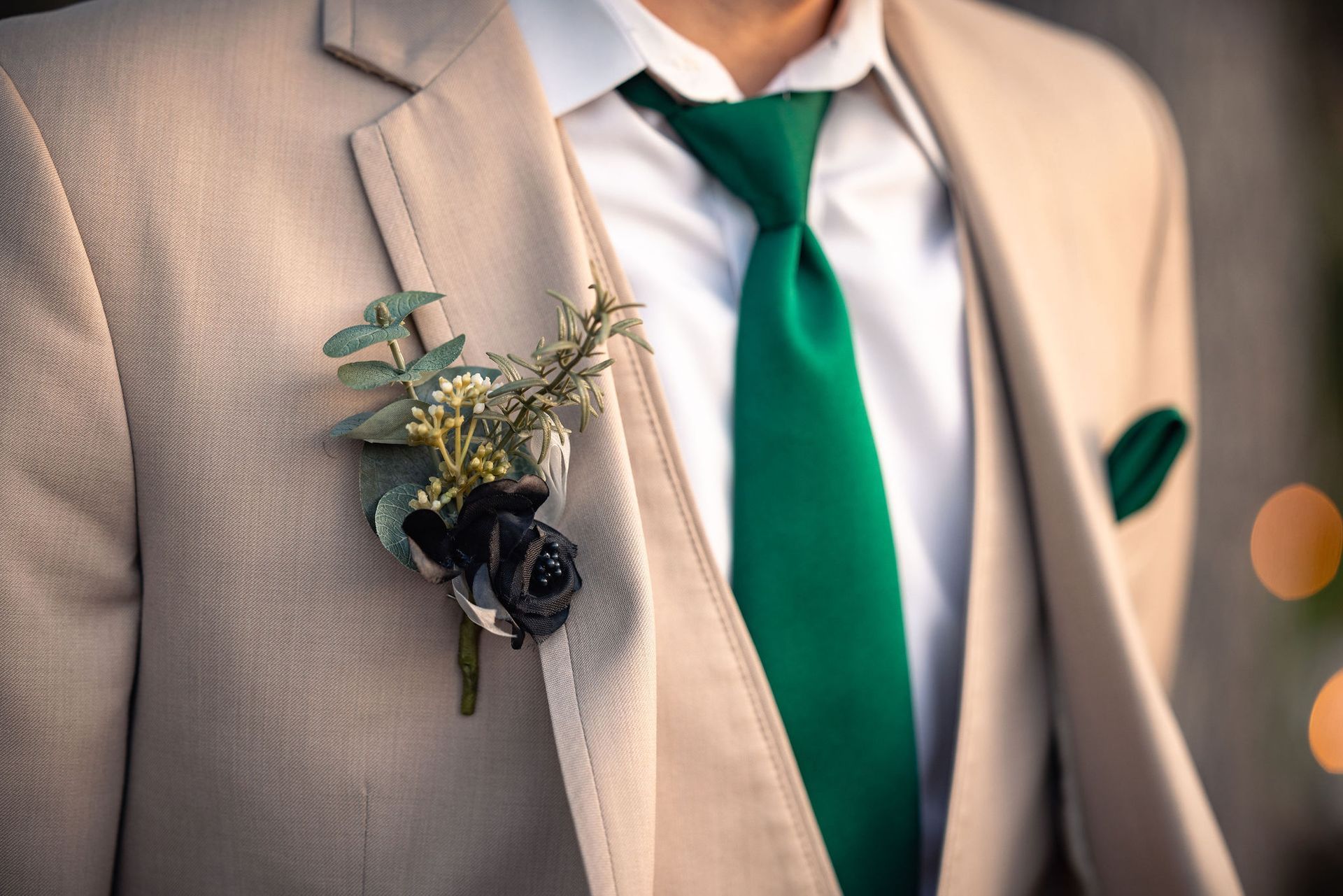Beige suit with a green tie and boutonniere. Pocket square, white shirt, and a formal setting are visible.