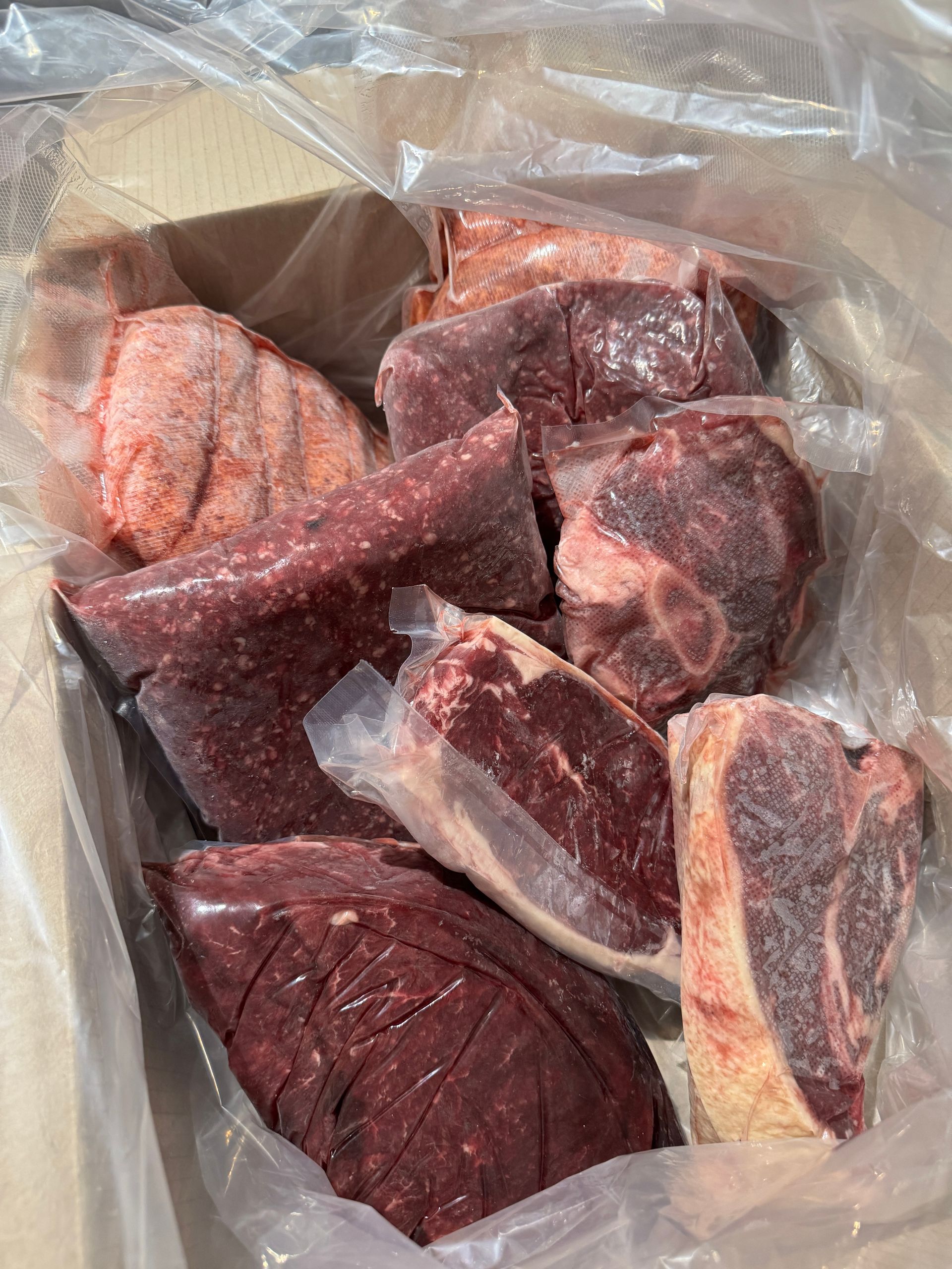 Assorted raw meat cuts in a plastic bag, including dark red and marbled pieces.