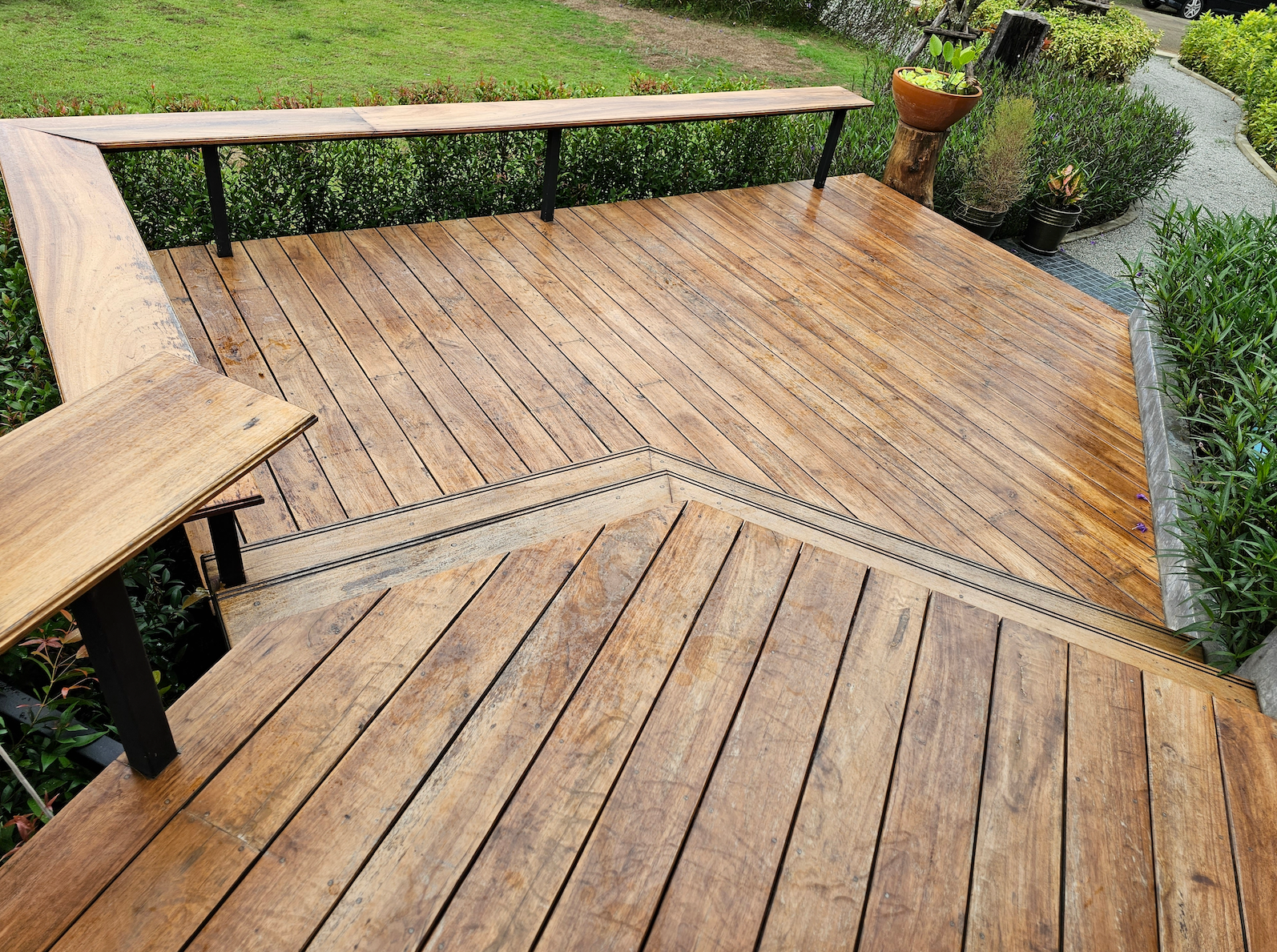 A wooden deck with a bench and stairs in a garden.