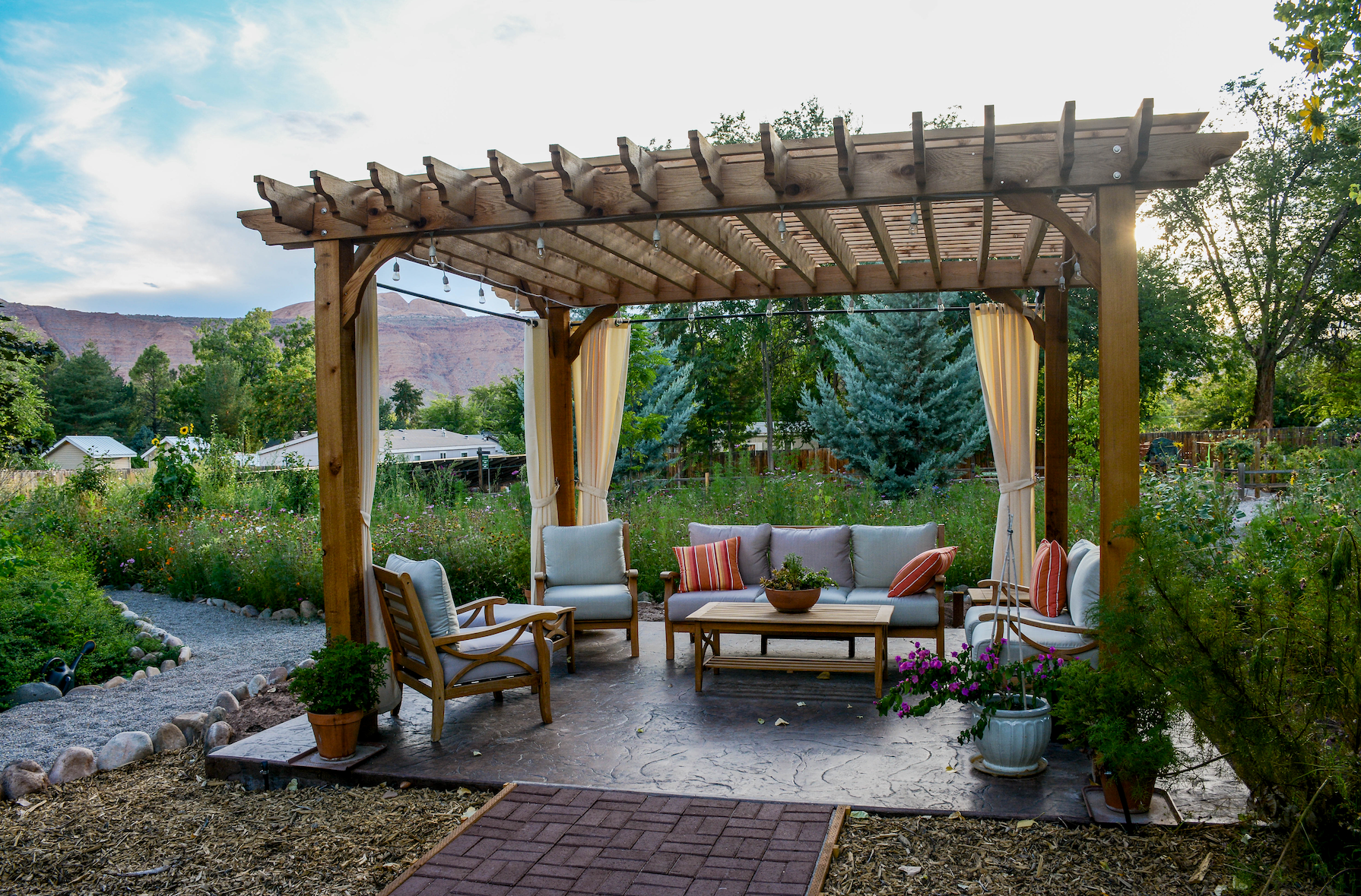 A wooden pergola with furniture underneath it in a garden.