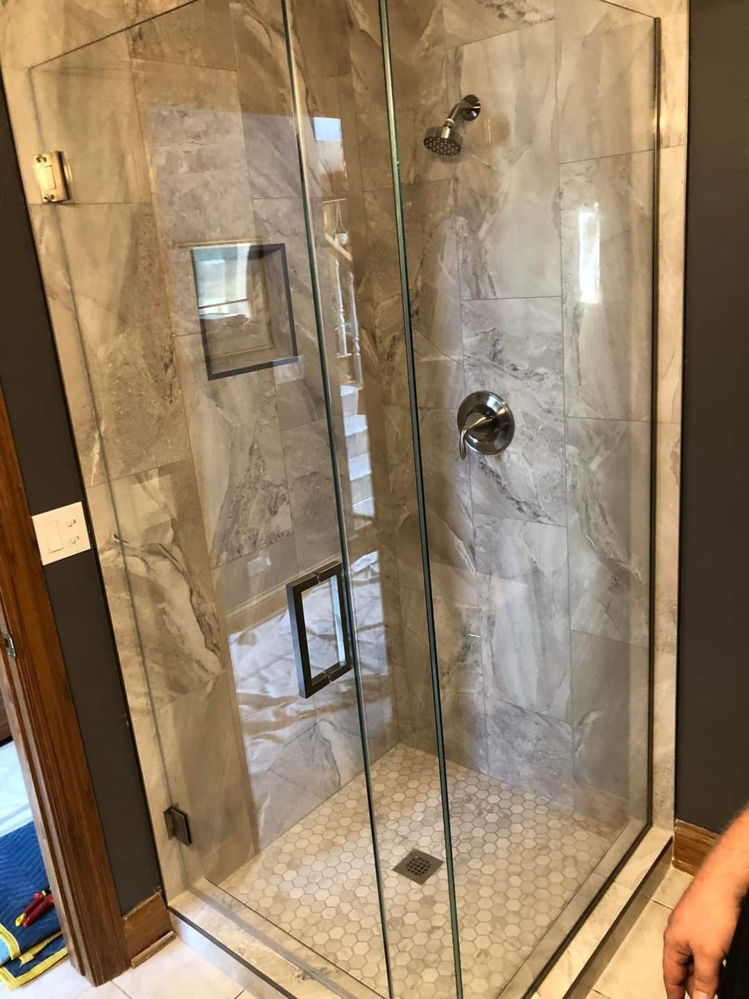 A person is standing in a bathroom next to a shower stall with a glass door.