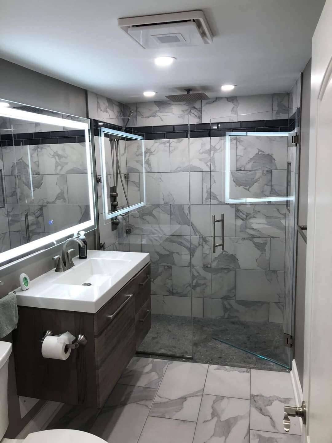 A bathroom with a sink , toilet , mirror and walk in shower.