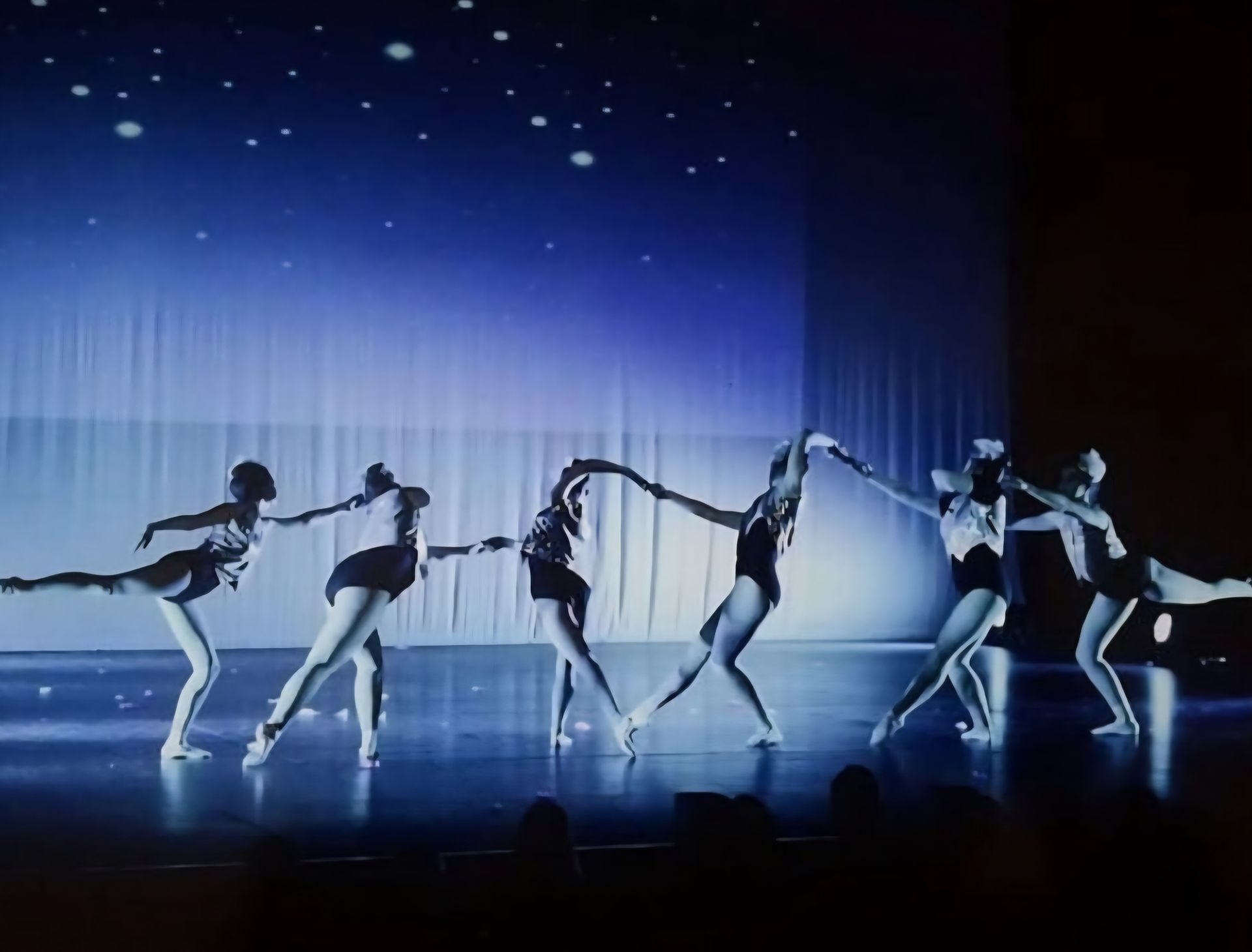 Dancers in black outfits form a chain against a starry blue backdrop on a stage.