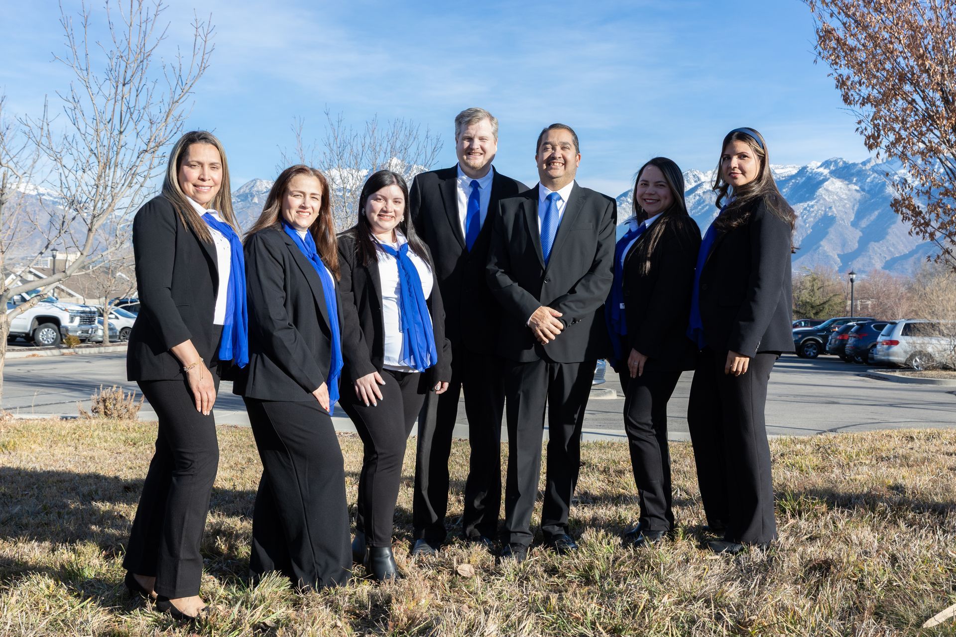 Group of people in business attire posing outdoors with mountains in the background.