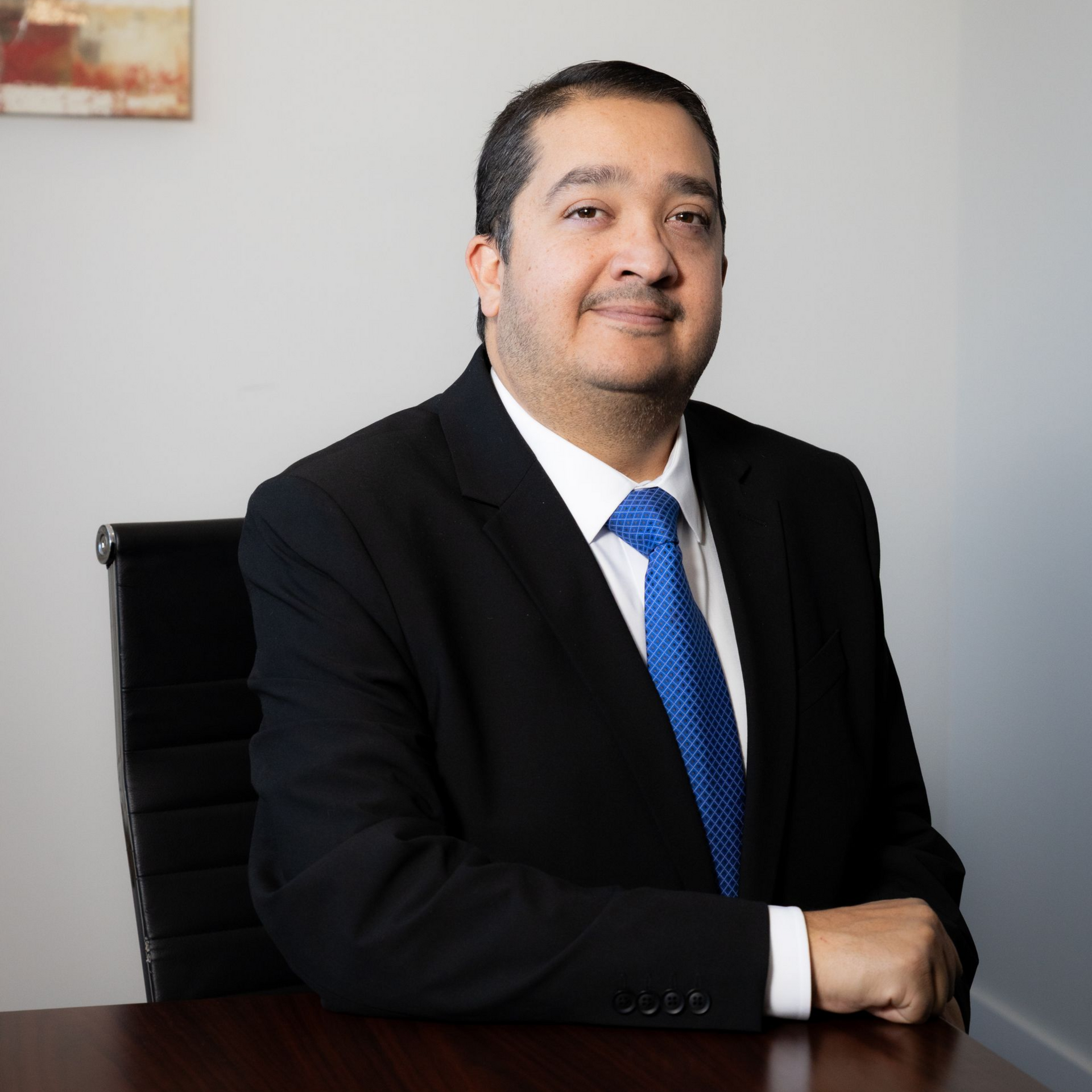 Man in a suit and blue tie sitting at a desk.