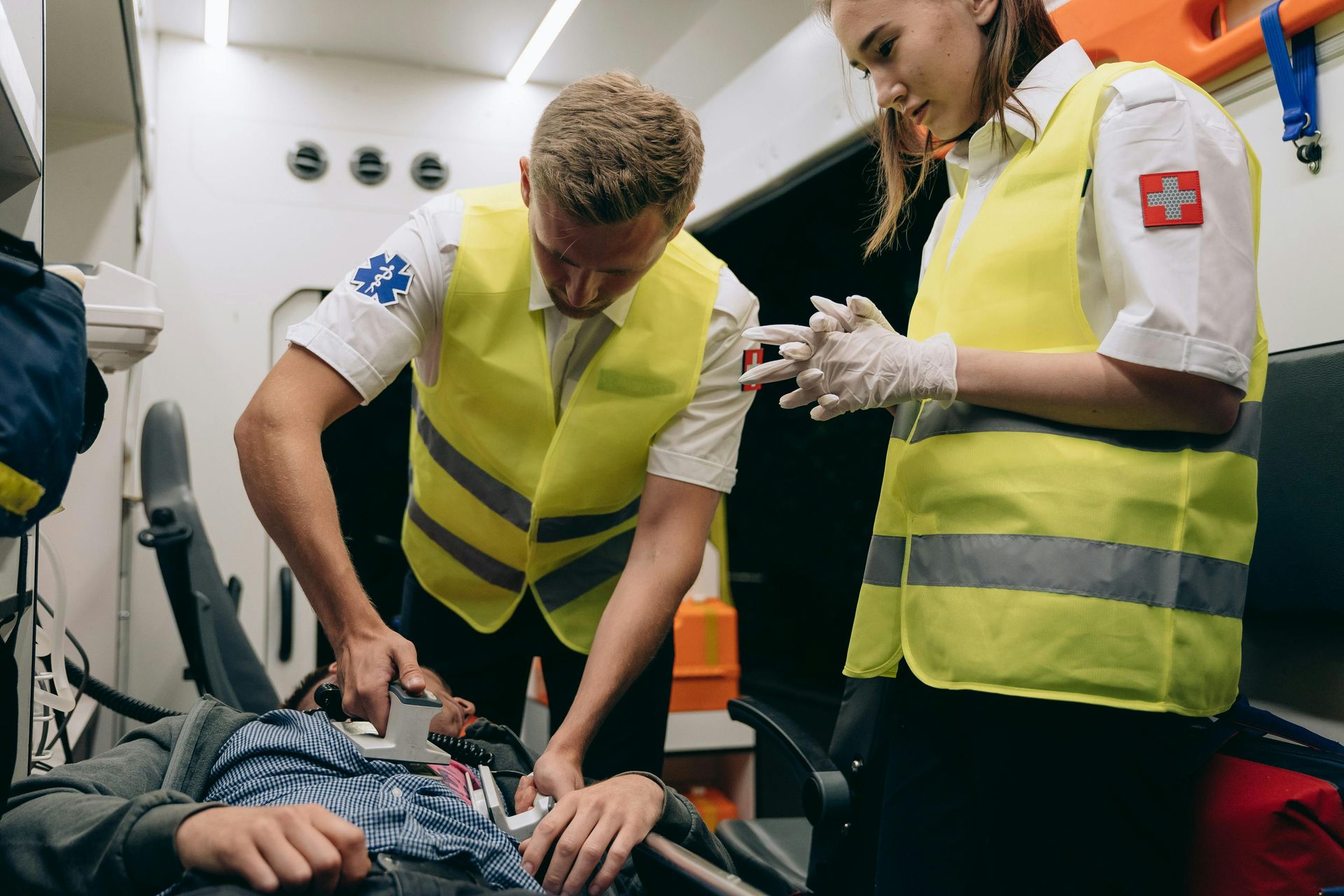 Paramedics tending to a patient on a stretcher inside an ambulance; one inserts a medical device.