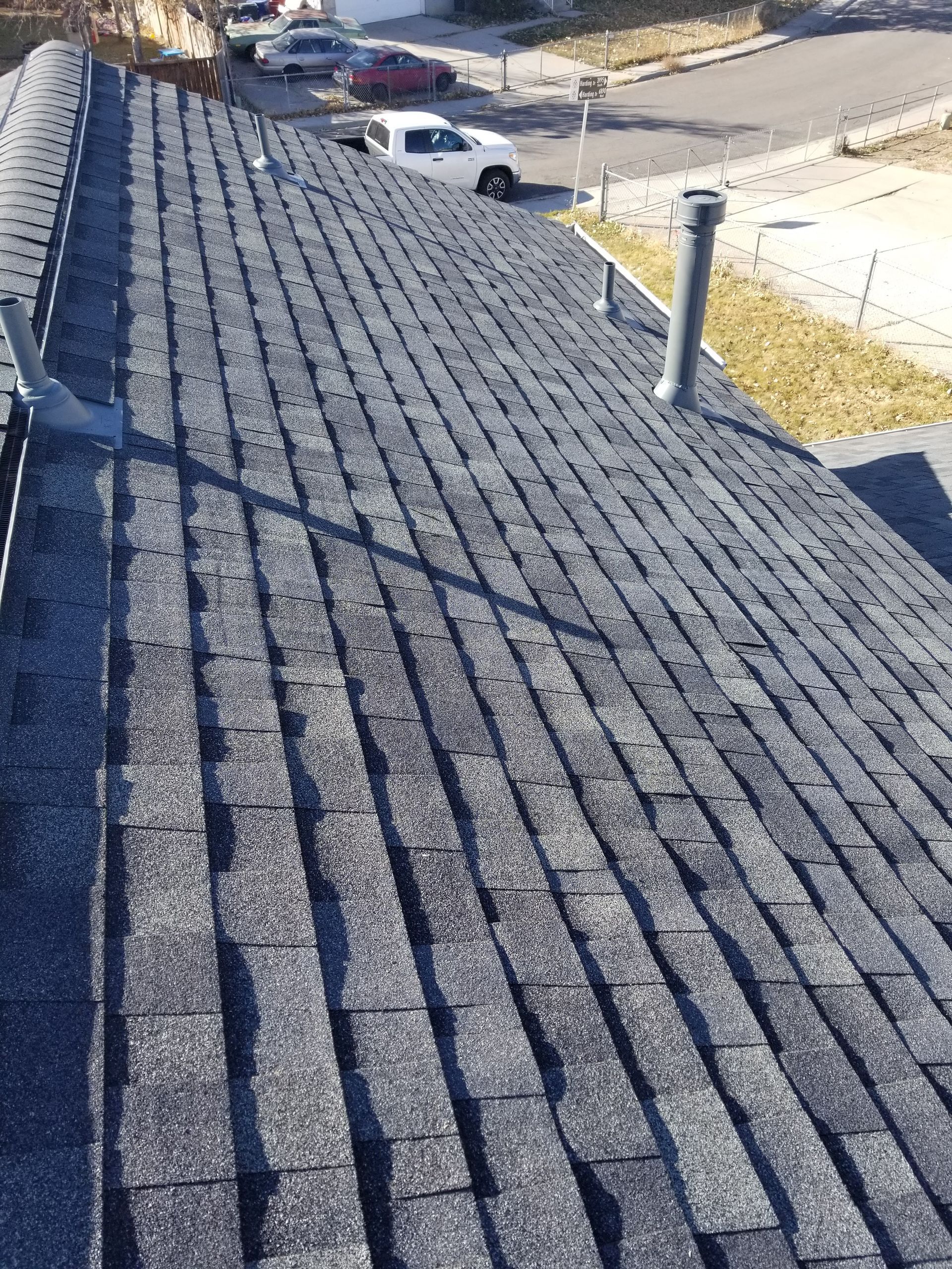Rooftop with gray shingles, vent pipes, and a distant street with parked cars below.