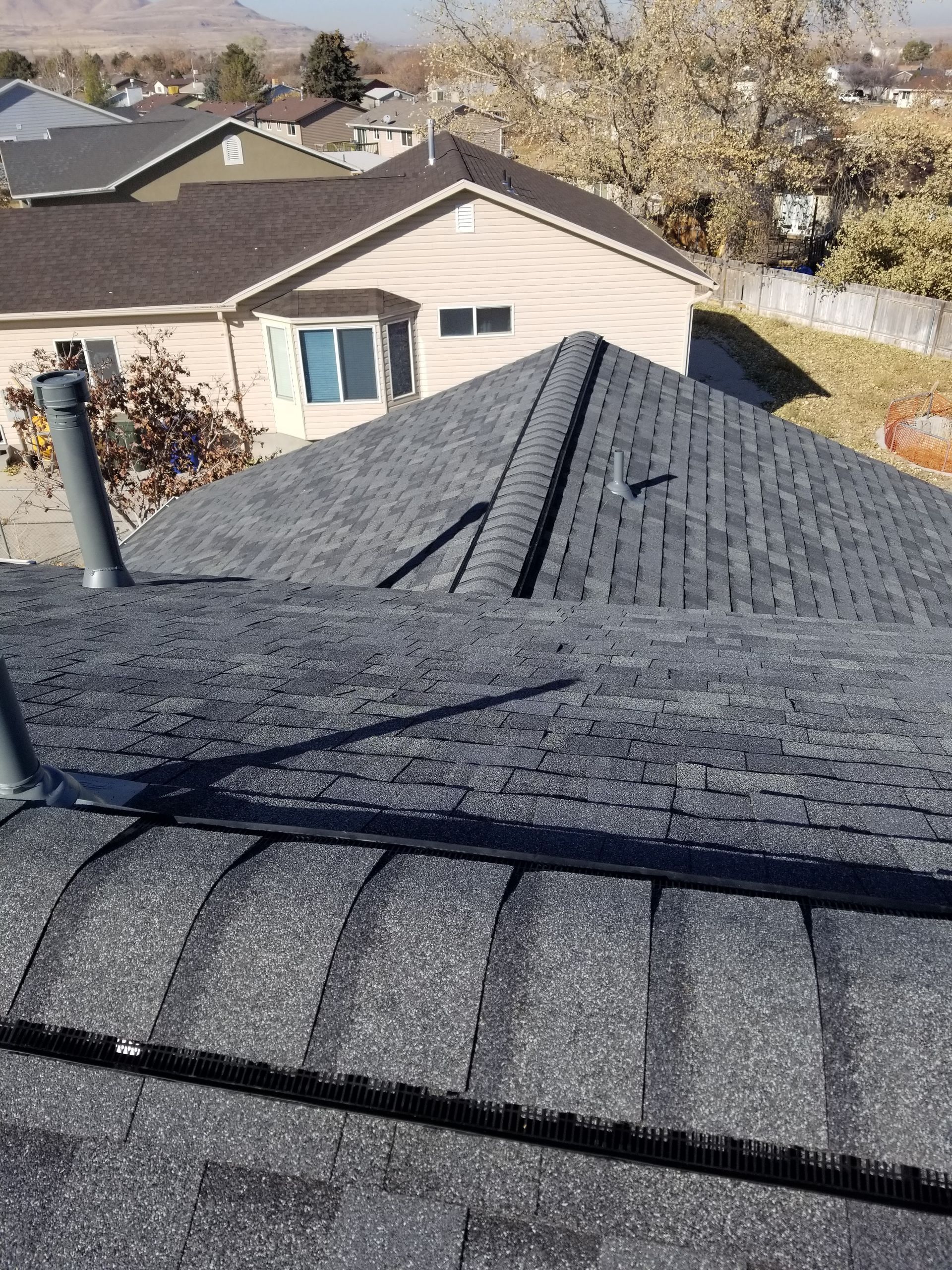 Roof with dark gray shingles and a vent pipe, viewed from above in a residential neighborhood