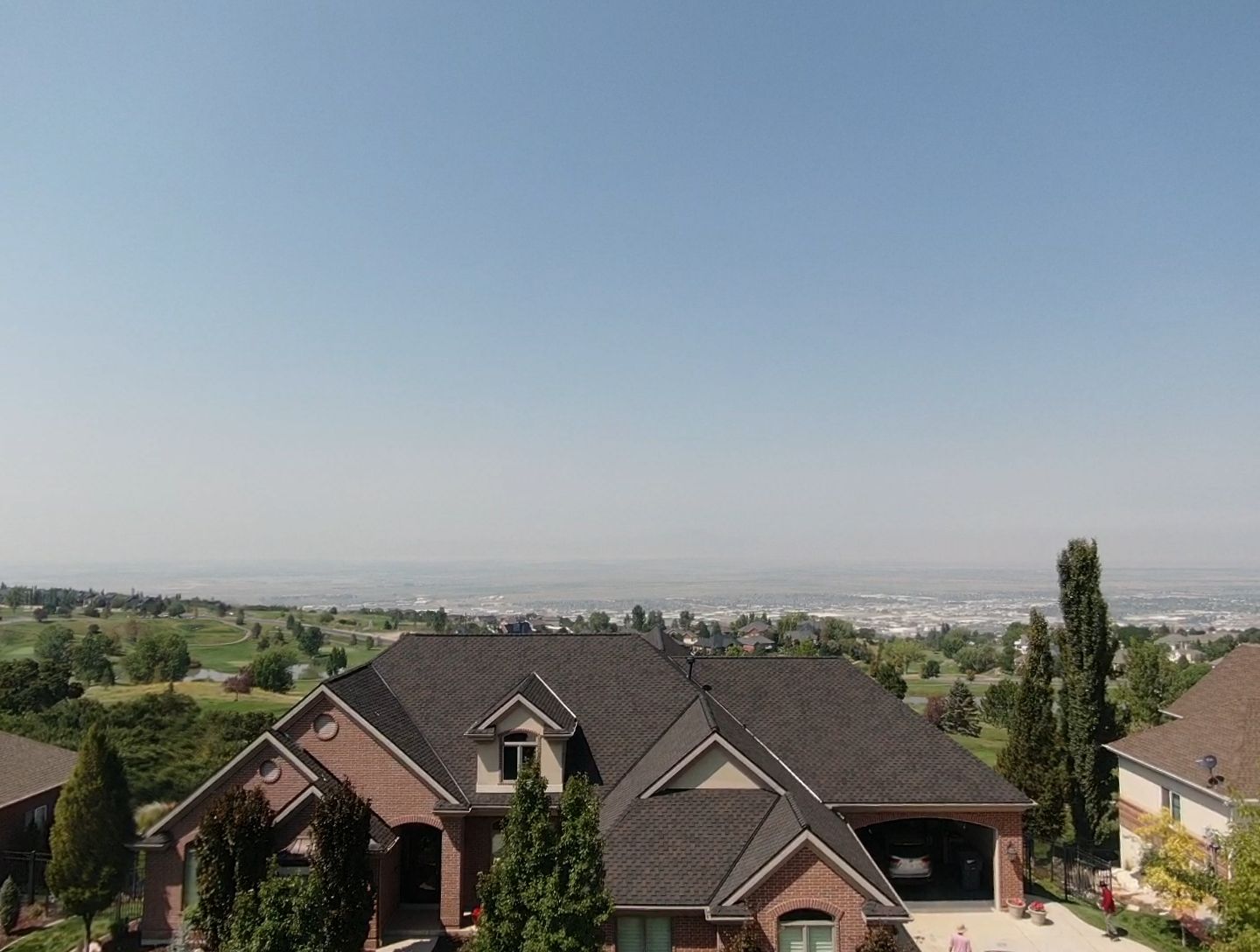 Suburban homes on a hillside overlooking a hazy city skyline under a clear blue sky