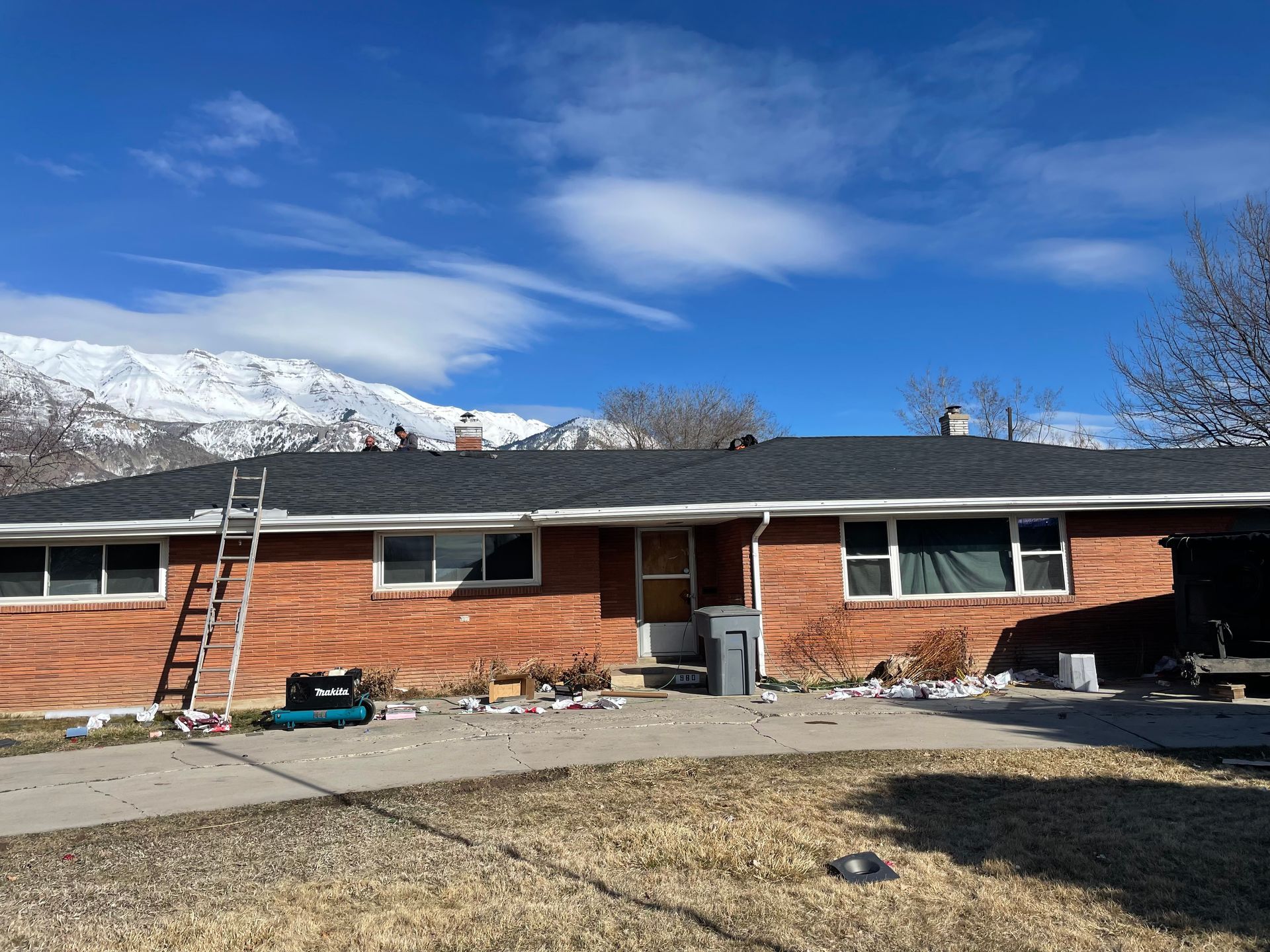 Single-story brick house with a ladder, snow-covered mountains, and a blue sky in the background