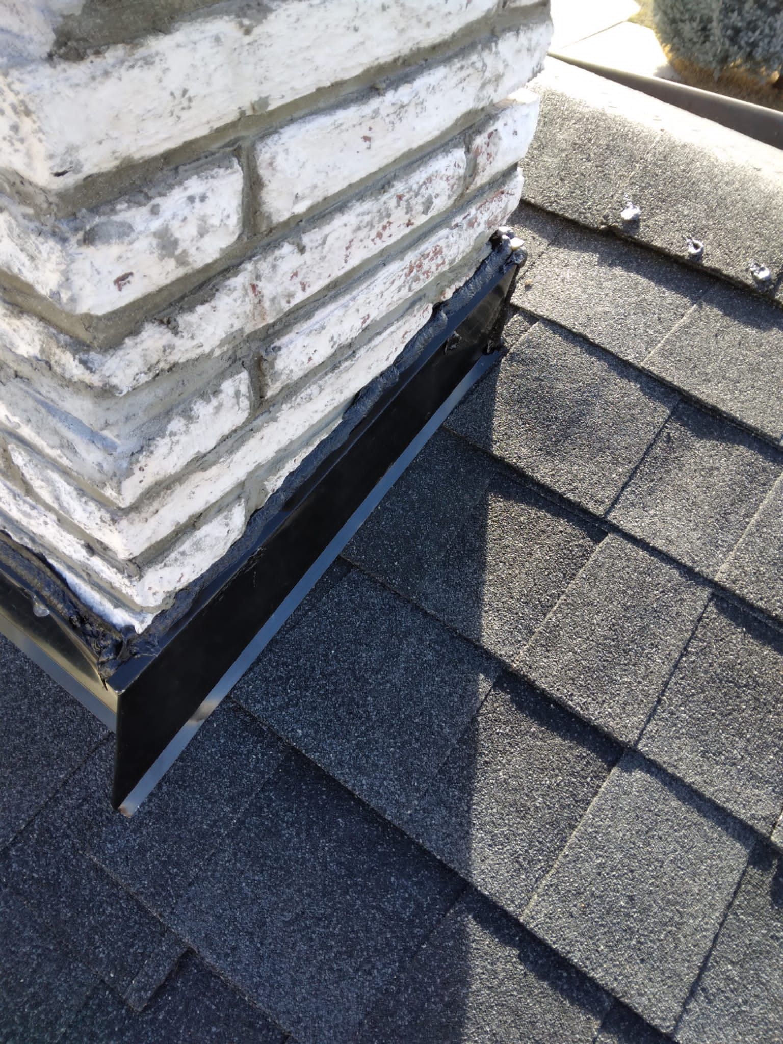 Close-up of a chimney flashing on a shingled roof beside a stone chimney.