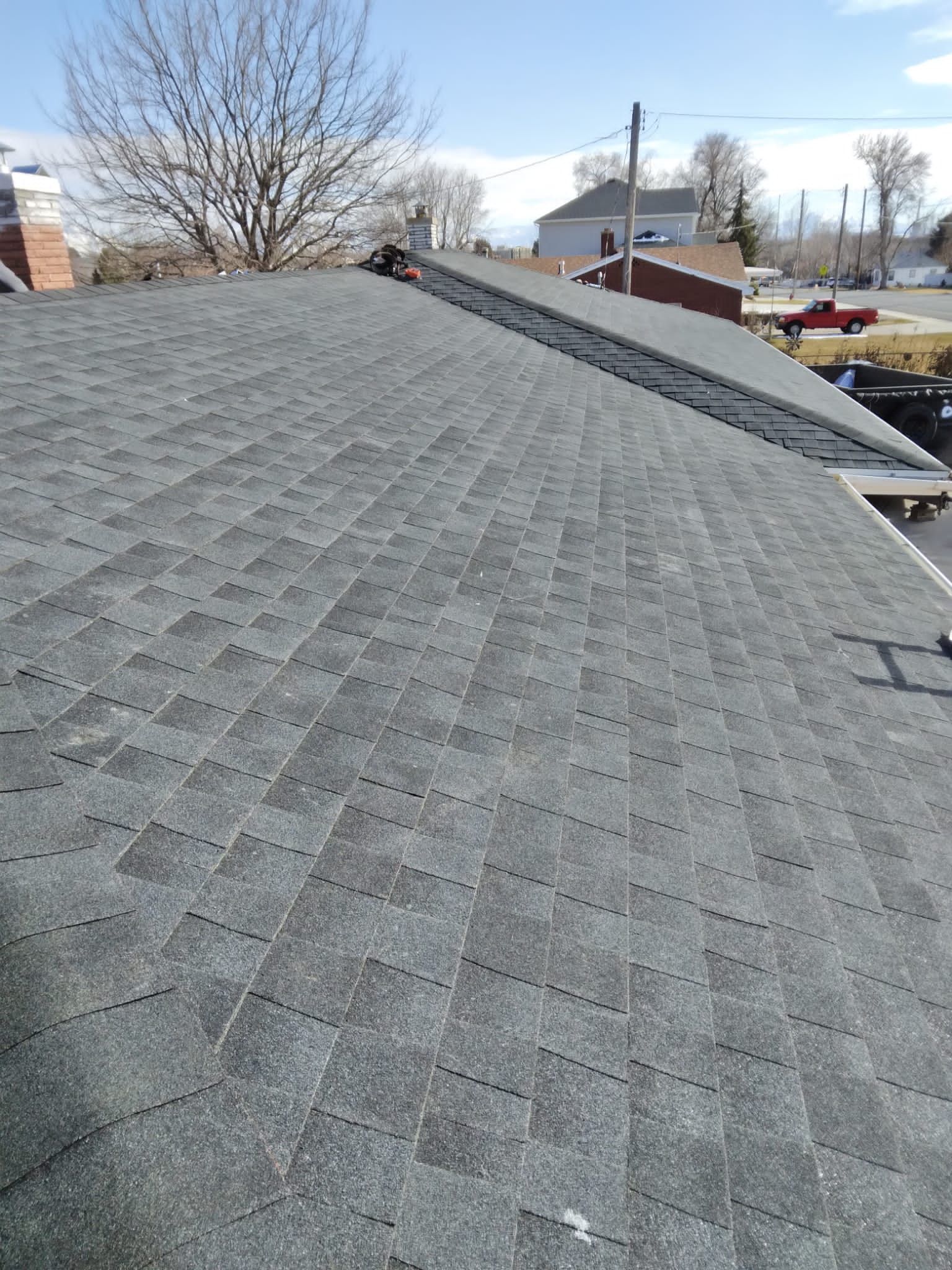 Gray shingled roof sloping toward houses and leafless trees under a clear sky