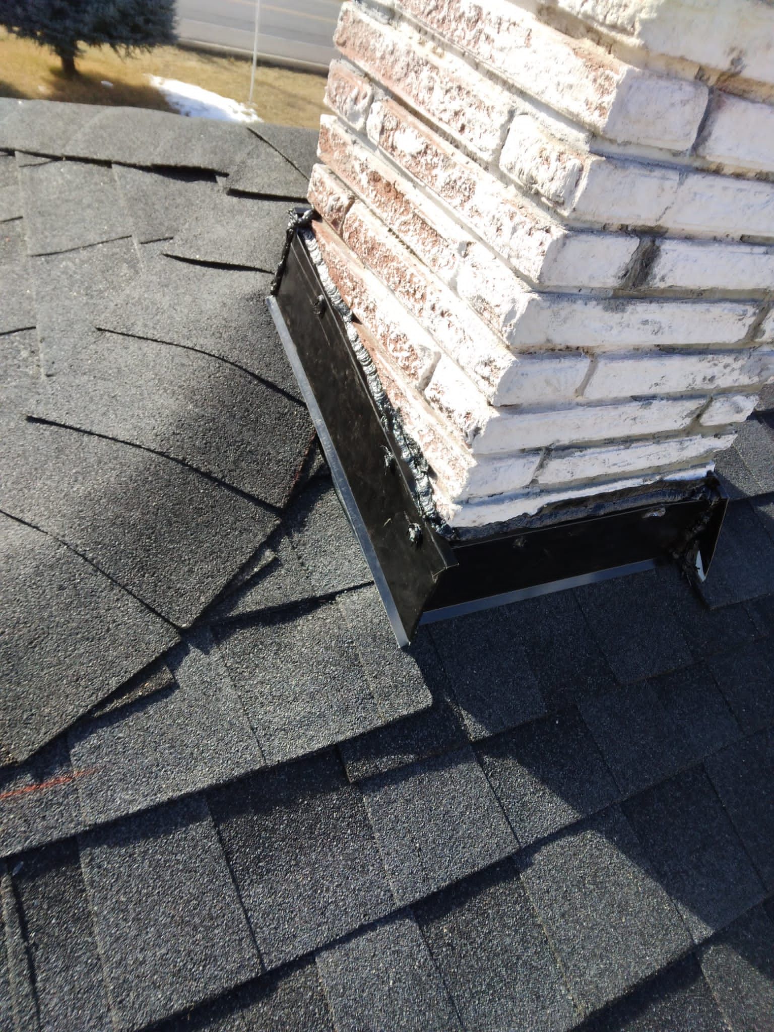 Roof shingles around a brick chimney with black flashing on a sloped roof