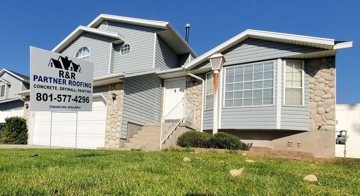 Damaged suburban house with a moved garage door and a “for sale” sign in the yard