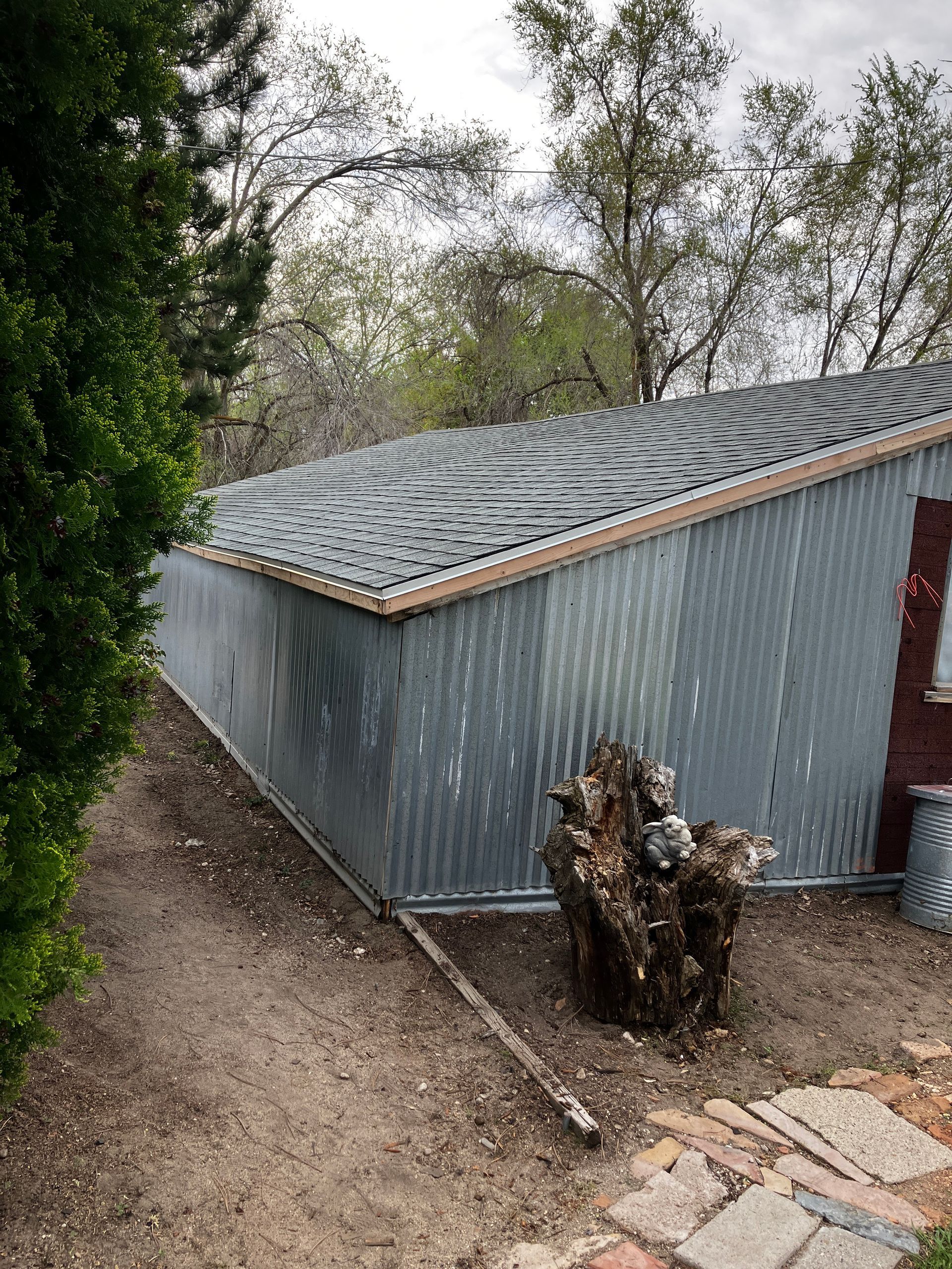 Gray corrugated shed on a hillside with trees and a stone path in the foreground
