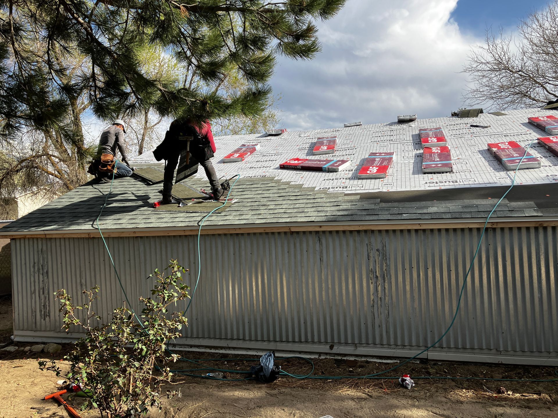 Workers on a roof under repair, with shingles and red tarp material visible.