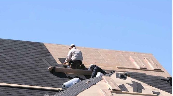 Worker repairing roof shingles on a house under a clear blue sky