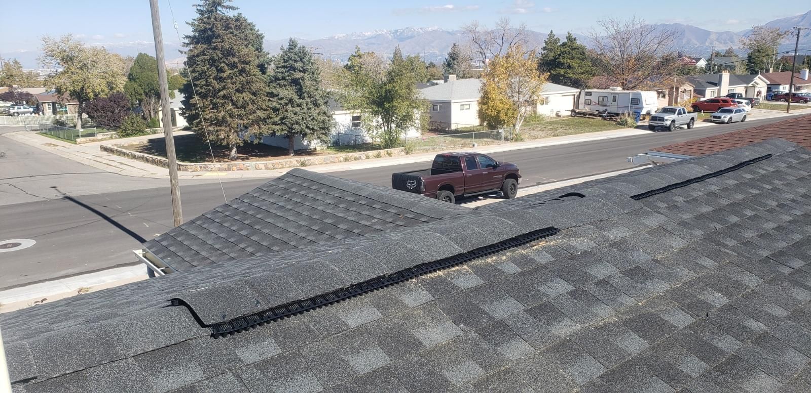 Rooftop view of a suburban street with a red SUV and trees under a clear sky.