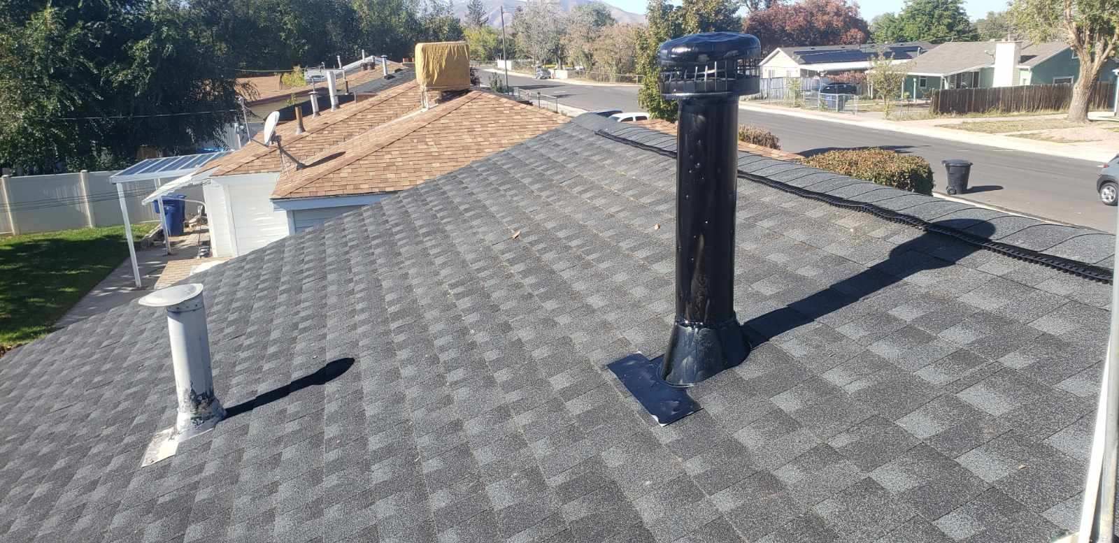Rooftop with dark shingles and a black vent pipe, viewed from above under bright daylight