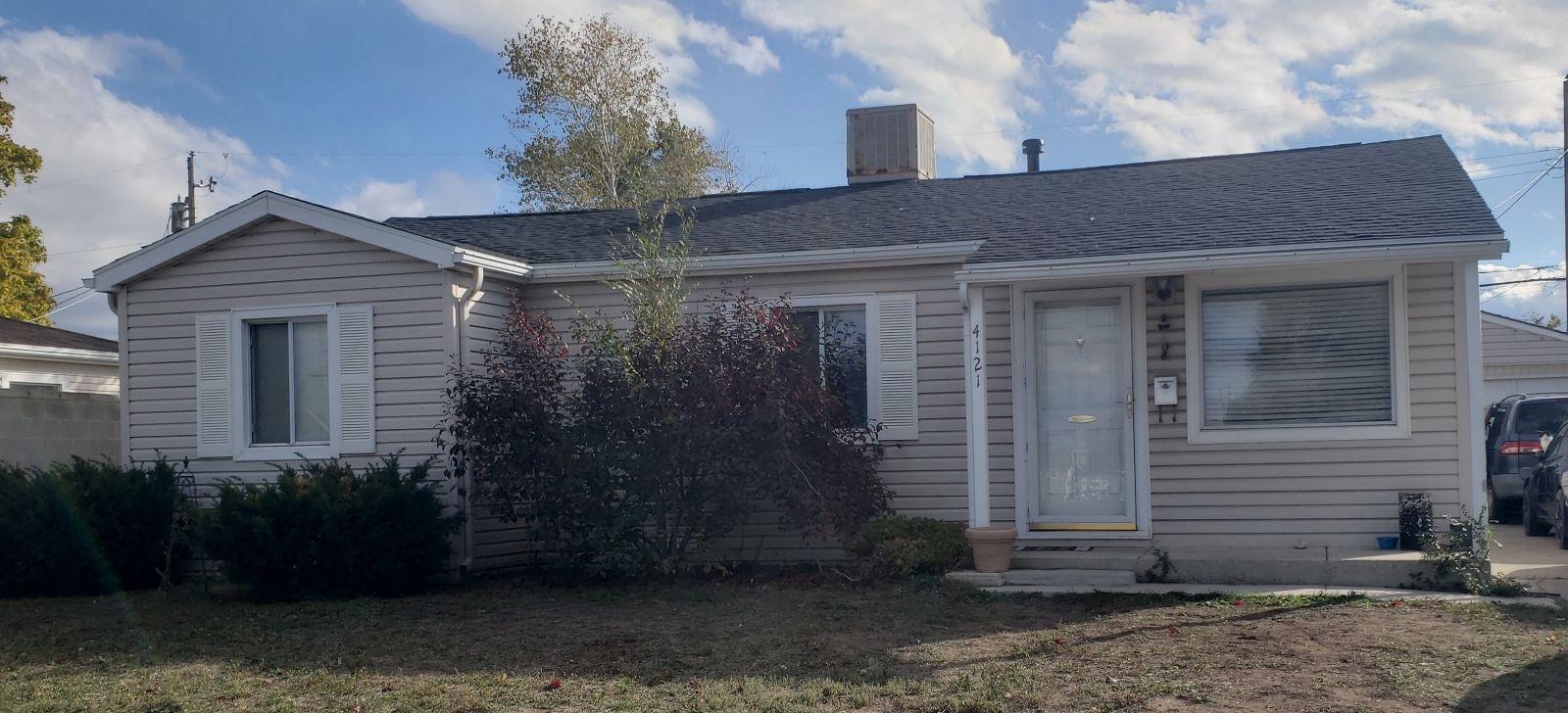 Single-story beige house with white trim and a small front porch under a partly cloudy sky