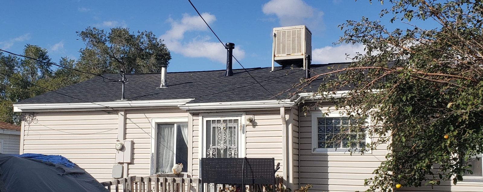 Single-story beige house with white trim, small front fence, and rooftop vent under a blue sky.