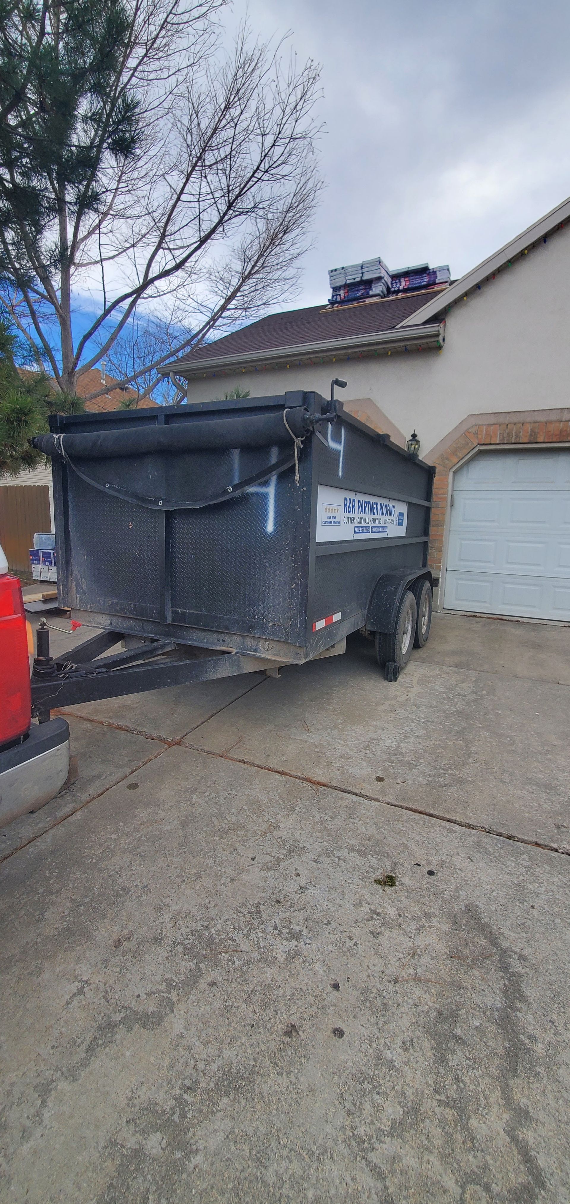 Damaged dumpster on a driveway beside a garage, with debris spilling out and a bent lid.