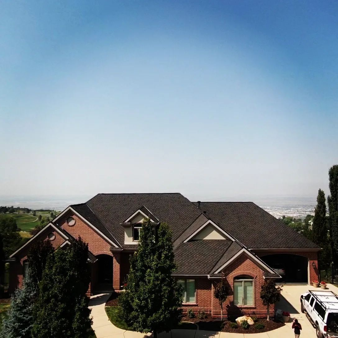 Large brick house with dark roof on a hillside under a clear blue sky
