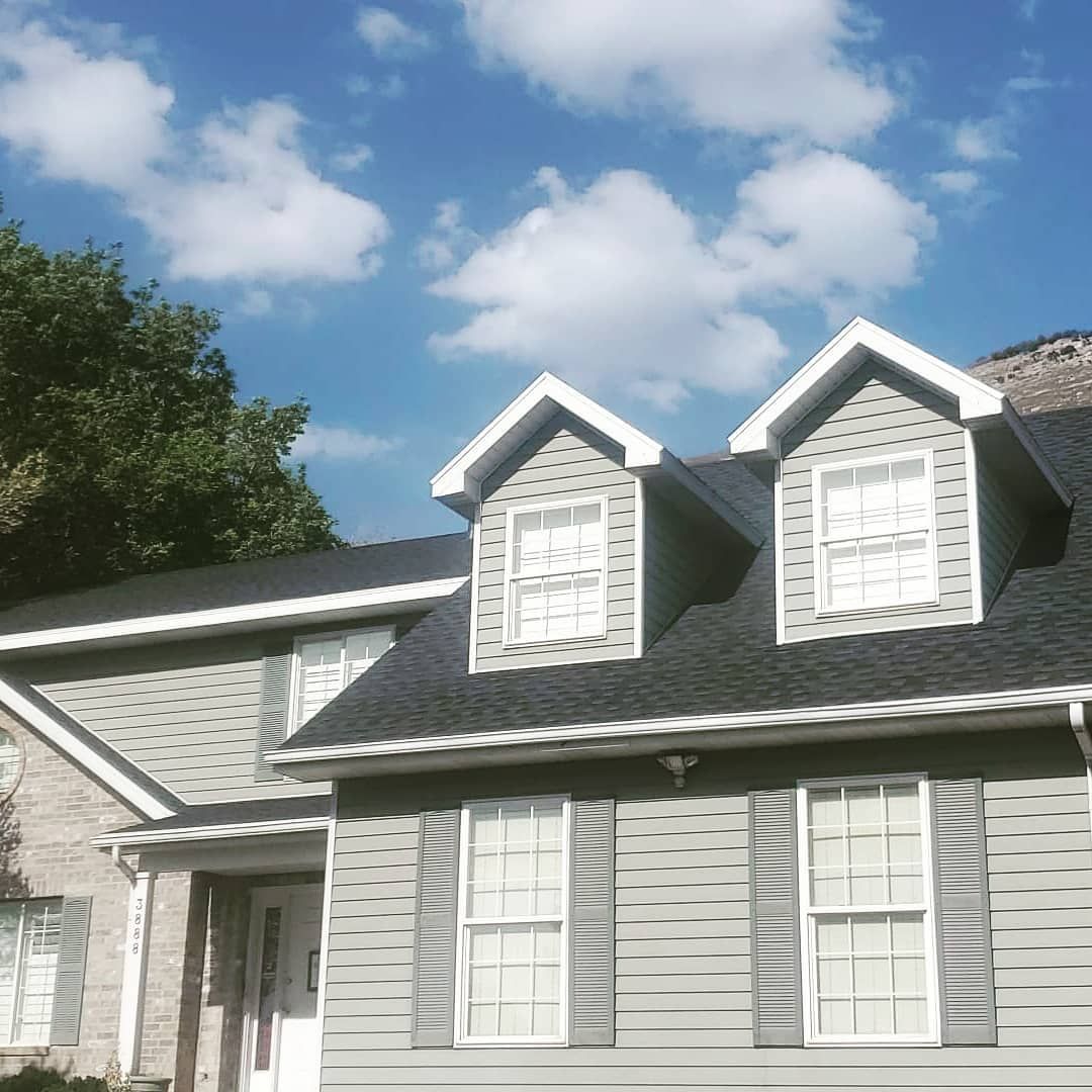 Gray house with white trim and dormer windows under a blue sky with clouds
