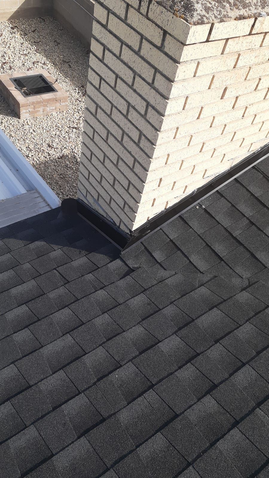 Dark gray shingle roof beside a light brick chimney and a flat gravel-roof edge