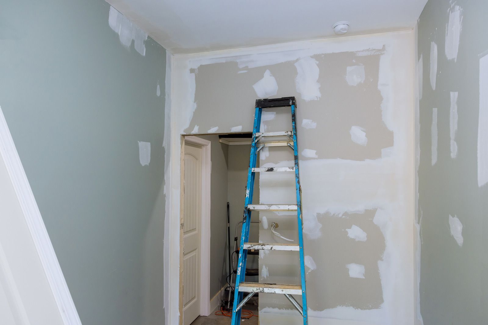 Small room under renovation with patched drywall and a blue ladder against the far wall