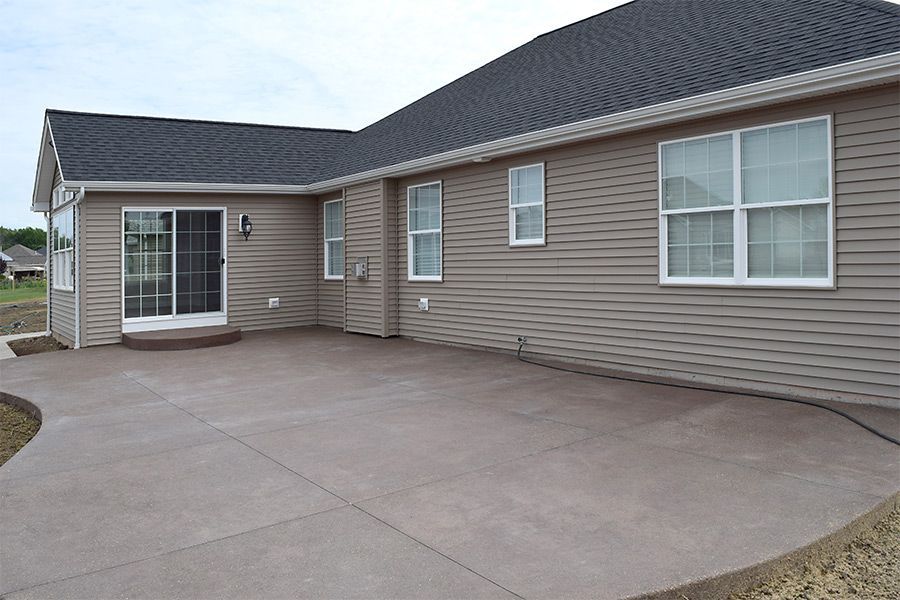 Concrete driveway and covered front entry of a single-story beige house with gray roof and siding.