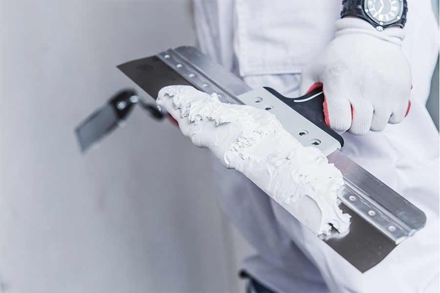 Gloved worker holding a squeegee with white sealant on a metal frame