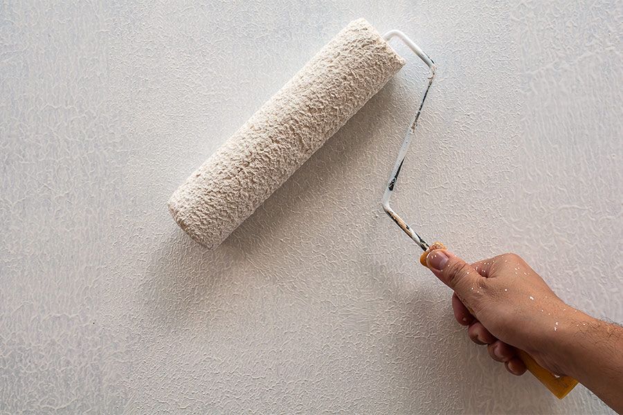 Hand rolling white paint on a wall with a paint roller and hand grip