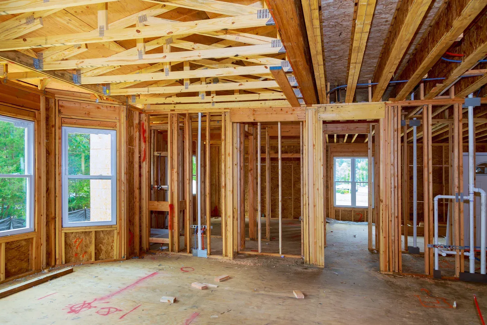 Unfinished wooden house interior with exposed framing, beams, windows, and open doorways