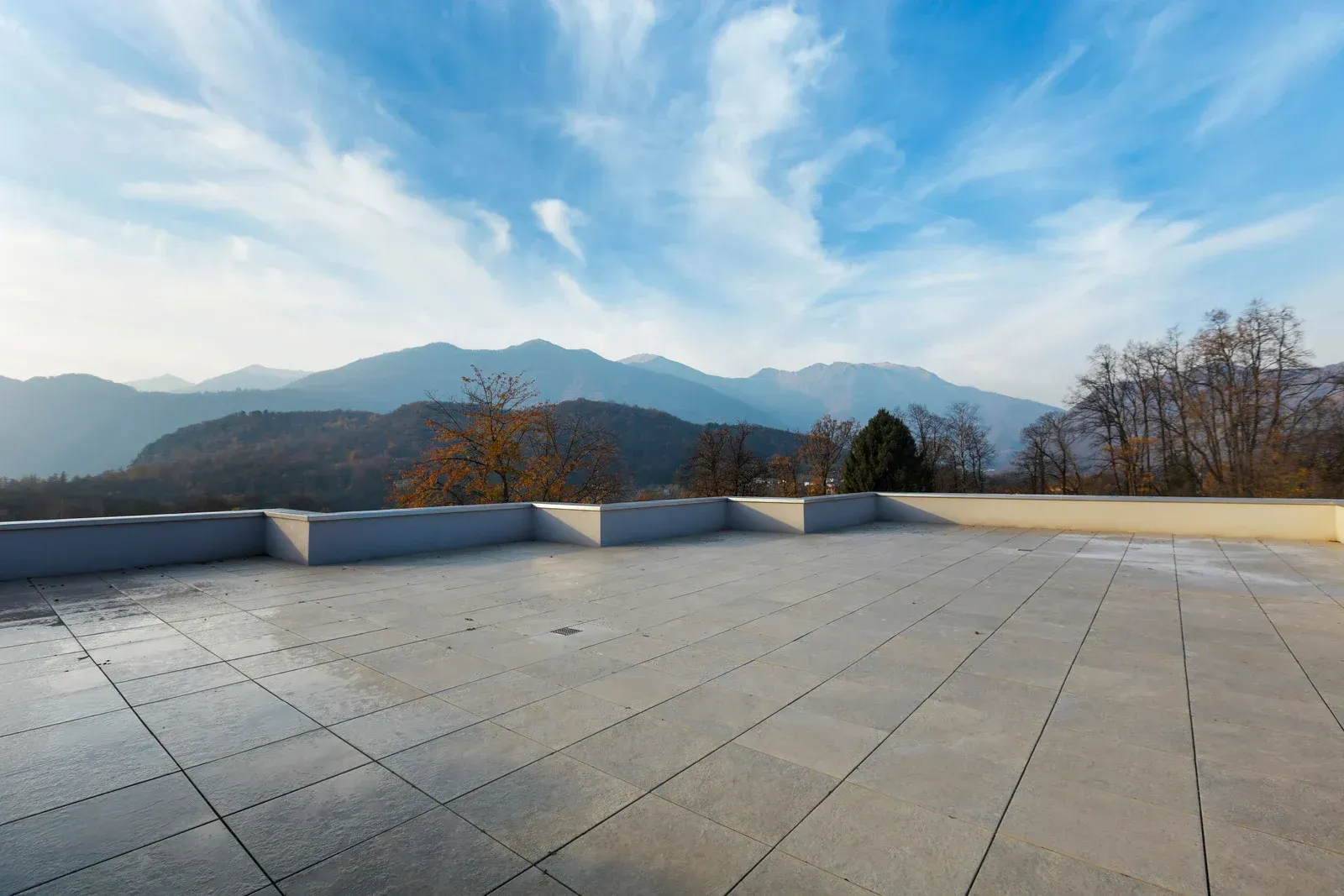 Wide stone terrace overlooking distant mountains under a bright blue sky with wispy clouds