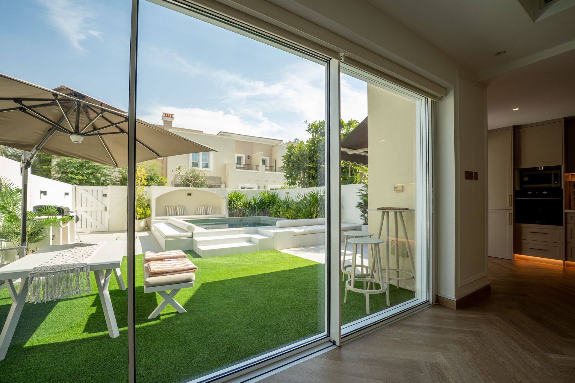 Modern living room opening to a sunny patio with green lawn, outdoor seating, and a large sliding glass door