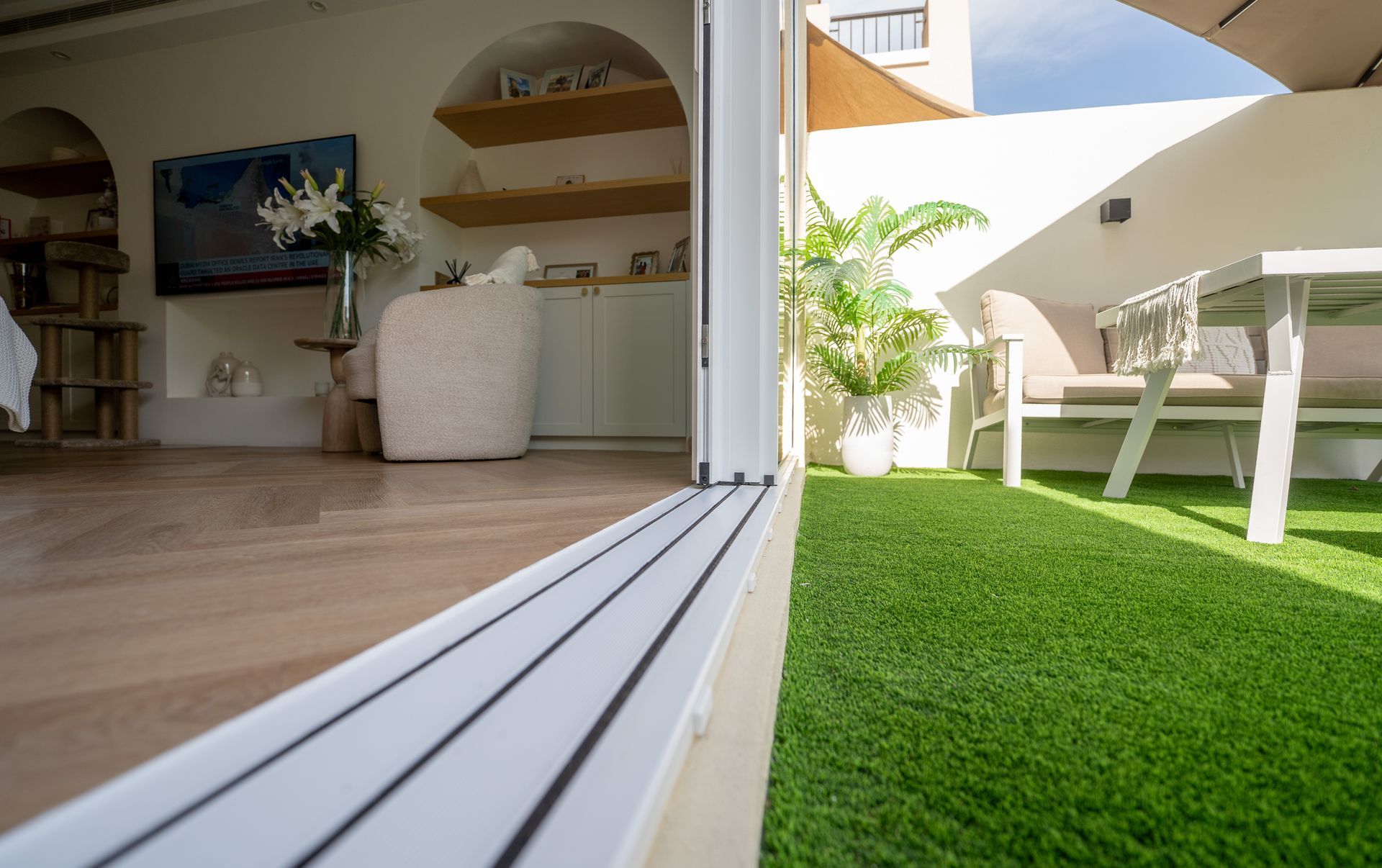 Modern patio with open sliding door, indoor seating, and white table on bright green artificial grass