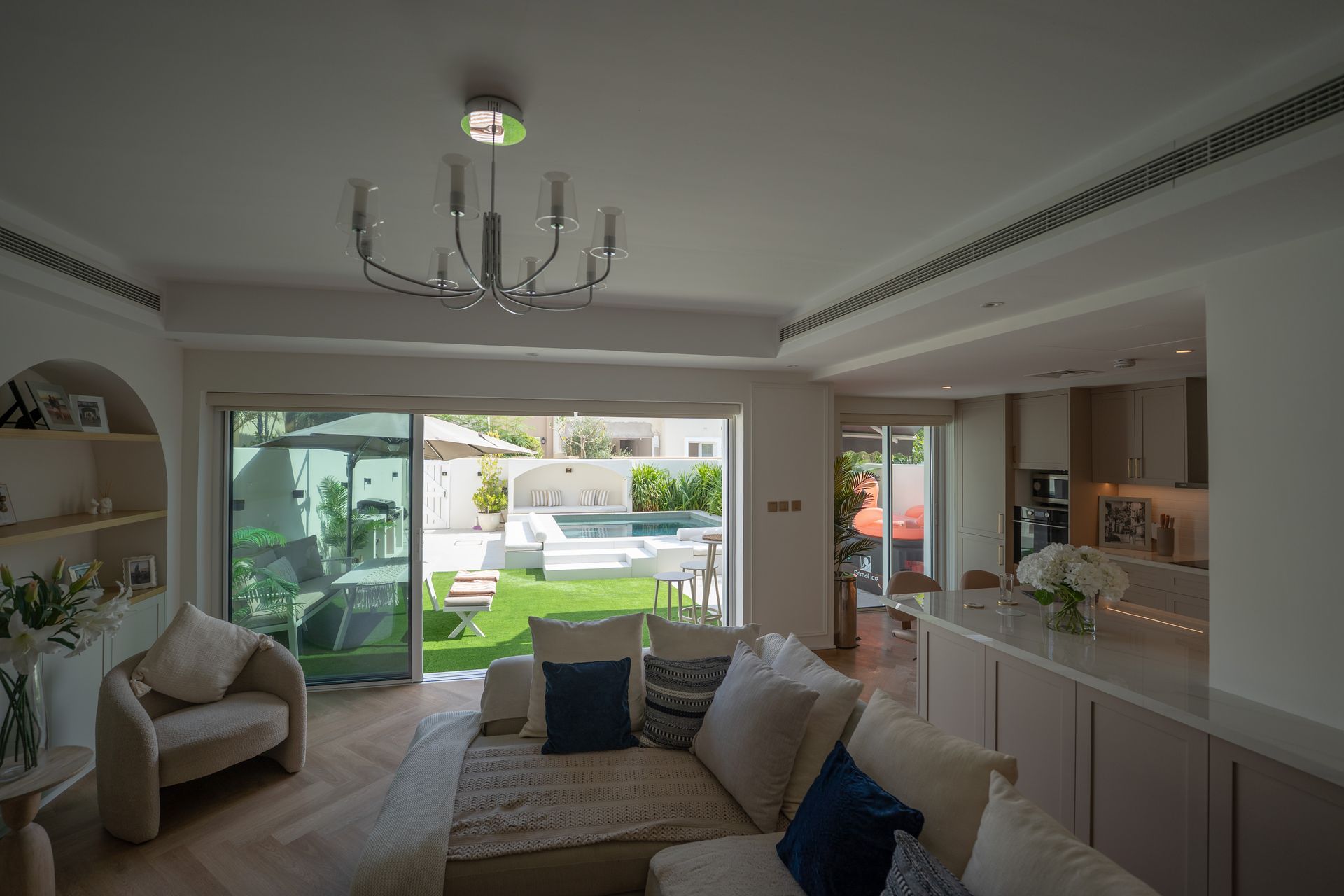Bright living room with sliding glass doors open to a sunny patio and garden, white sofa, and chandelier