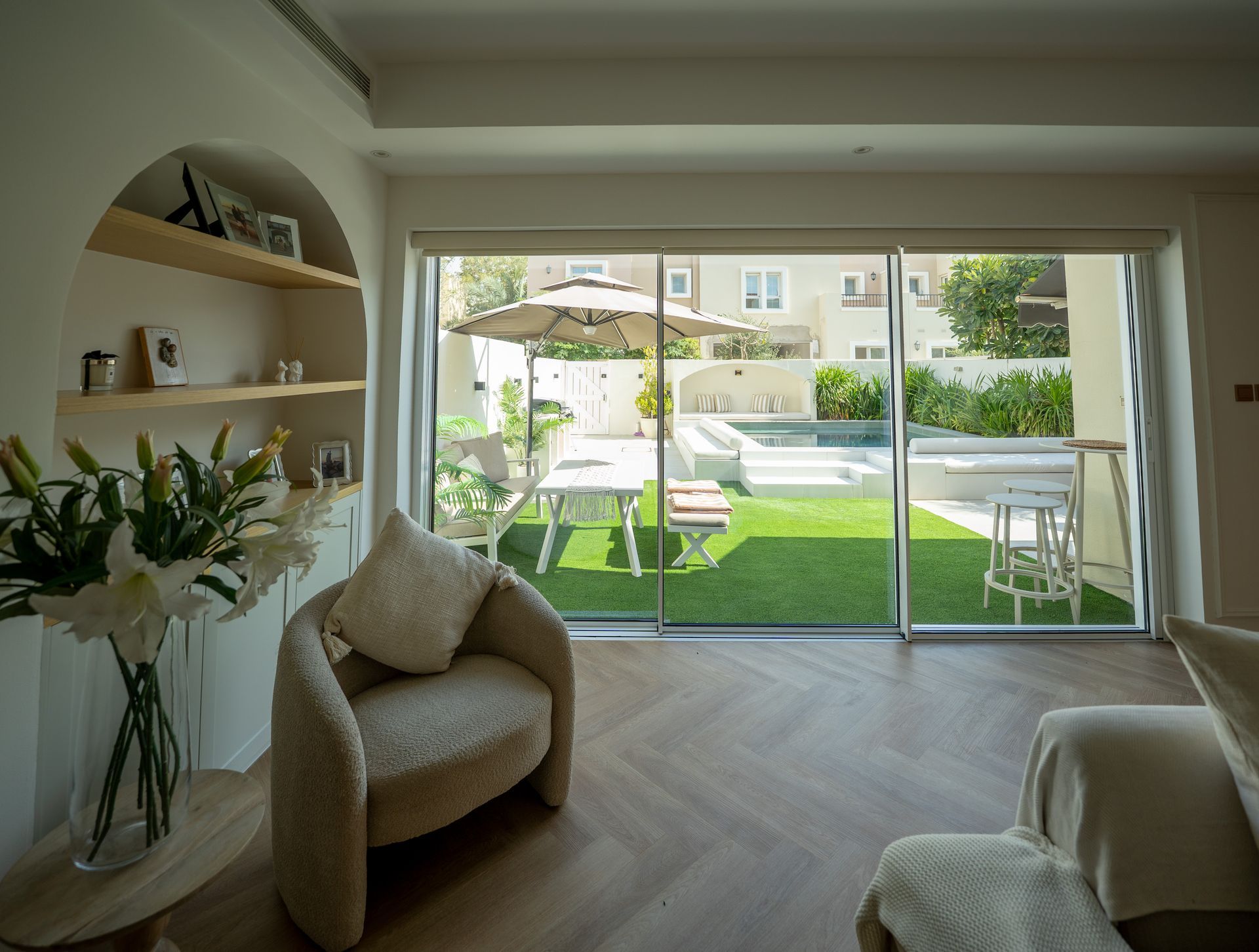 Bright living room with arched shelves, wicker chair, and sliding doors opening to a sunny patio and lawn