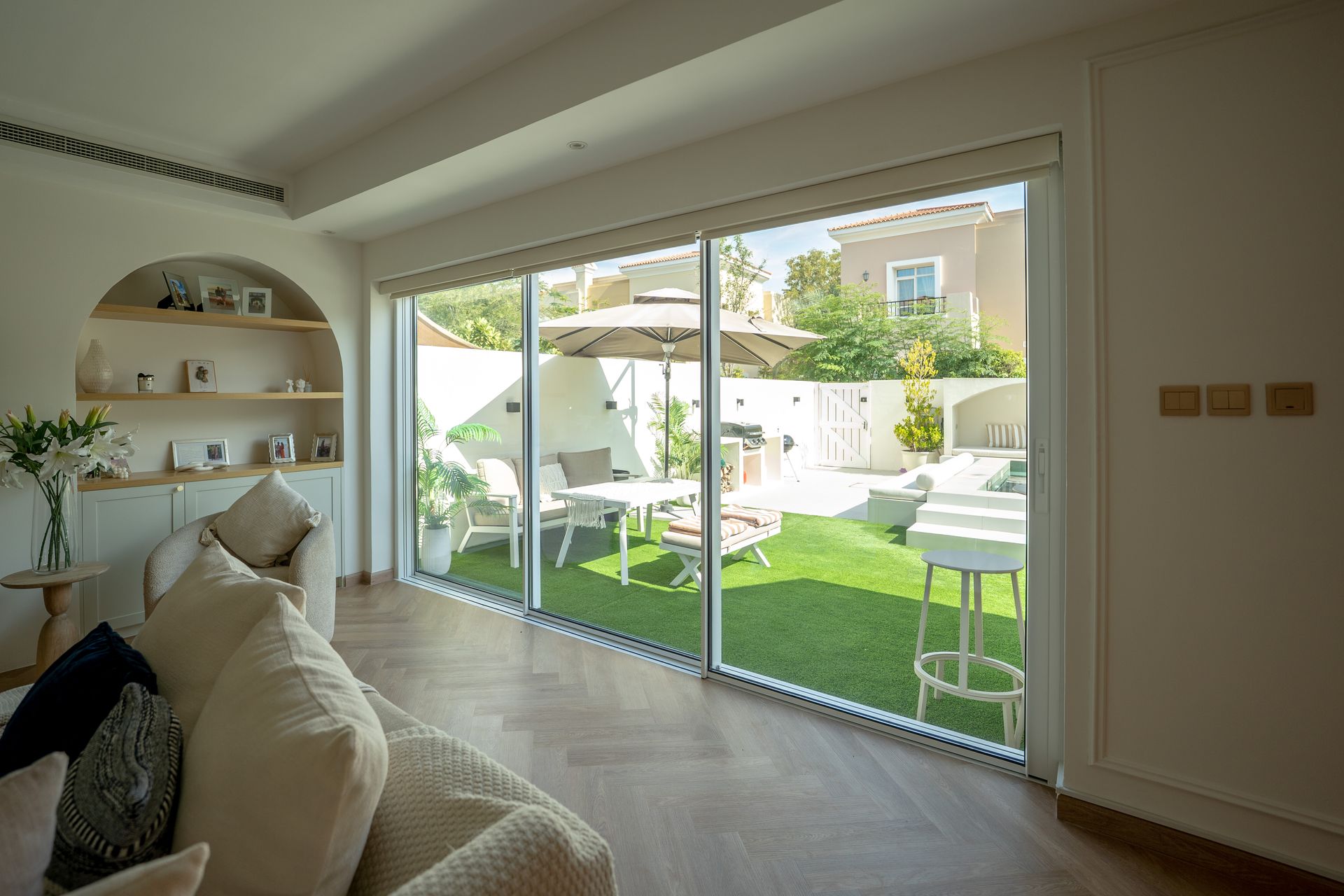 Bright living room opening to a sunlit patio with sliding glass doors and green lawn beyond