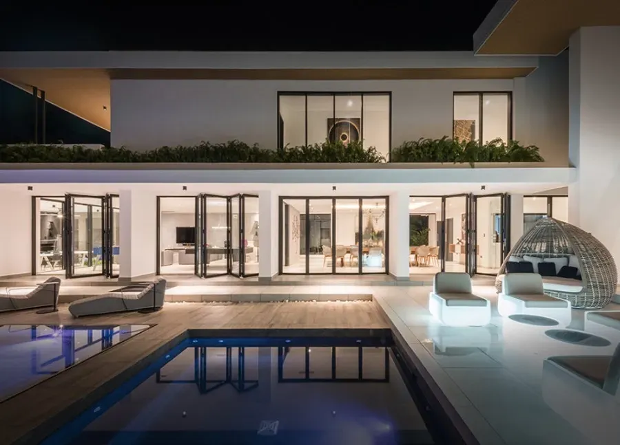 A large house with a swimming pool in front of it at night.