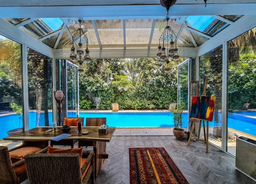 A room with a table and chairs and a swimming pool in the background.