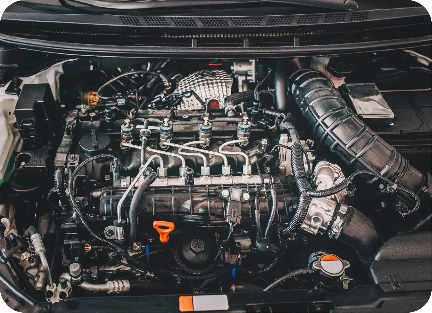 A high-angle view of a clean car engine bay showing various mechanical components, hoses, and an orange oil dipstick handle.
