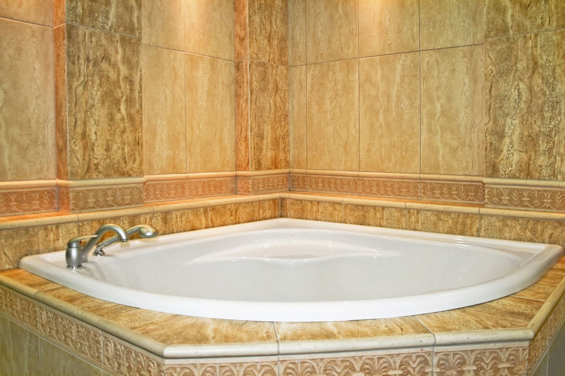 Corner bathtub with beige tile surround and faucet.