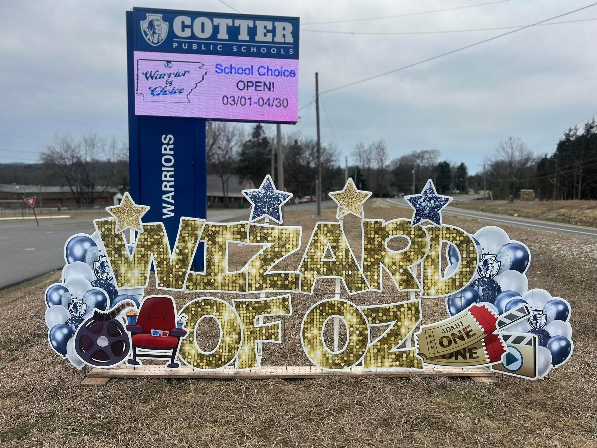 Wizard of Oz holiday display with gold letters, stars, snowmen, and a Cotter School sign by the roadside