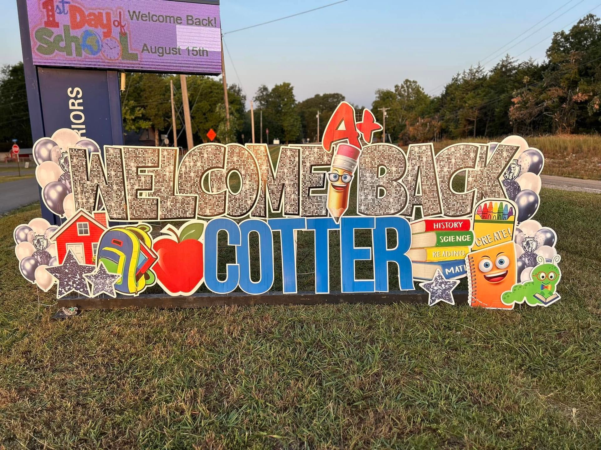 School-themed “Cutter” sign display on grass with colorful cartoon cutouts and a “1 Day” banner