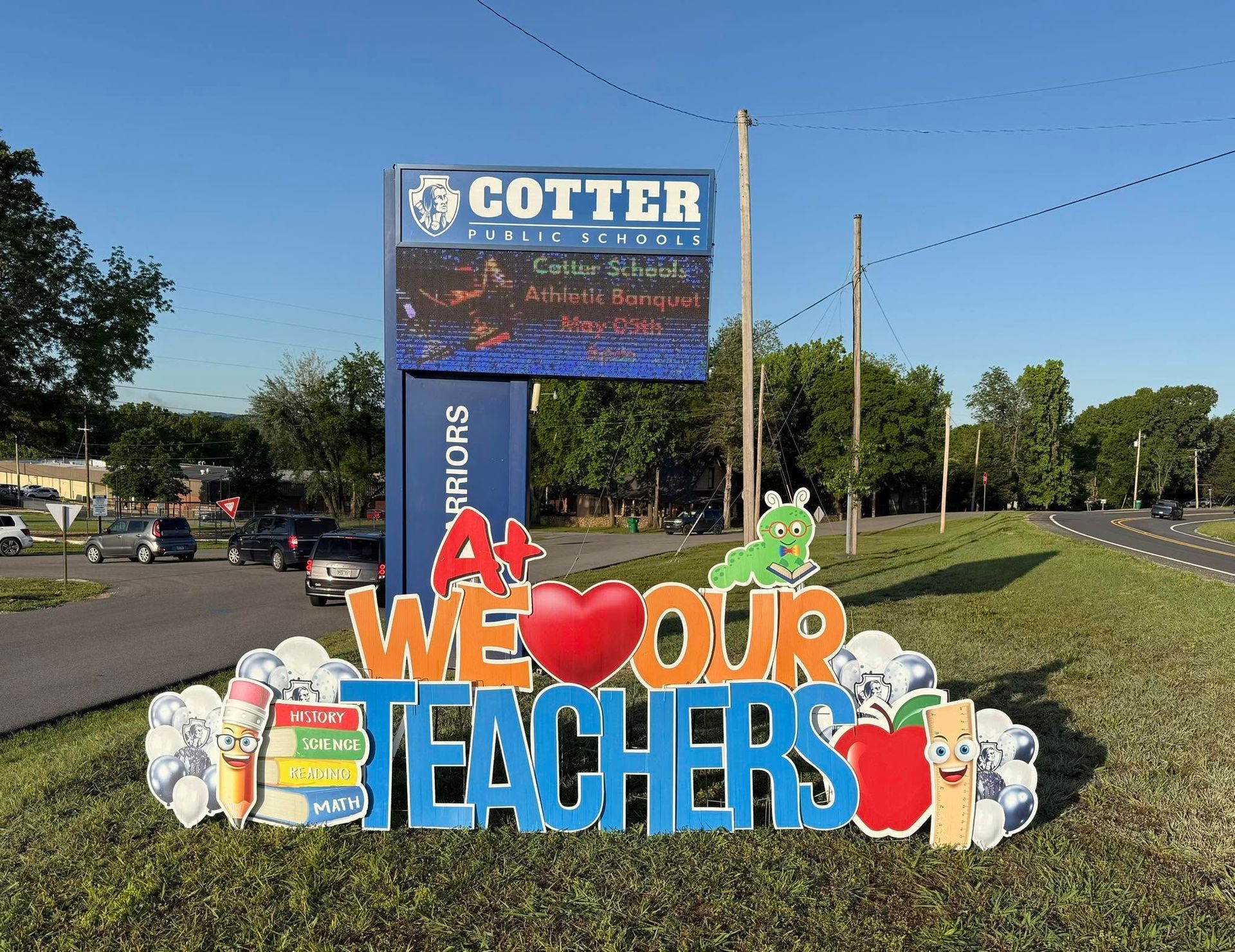 Colorful roadside sign reading “We love our teachers” in front of Gotter school grounds