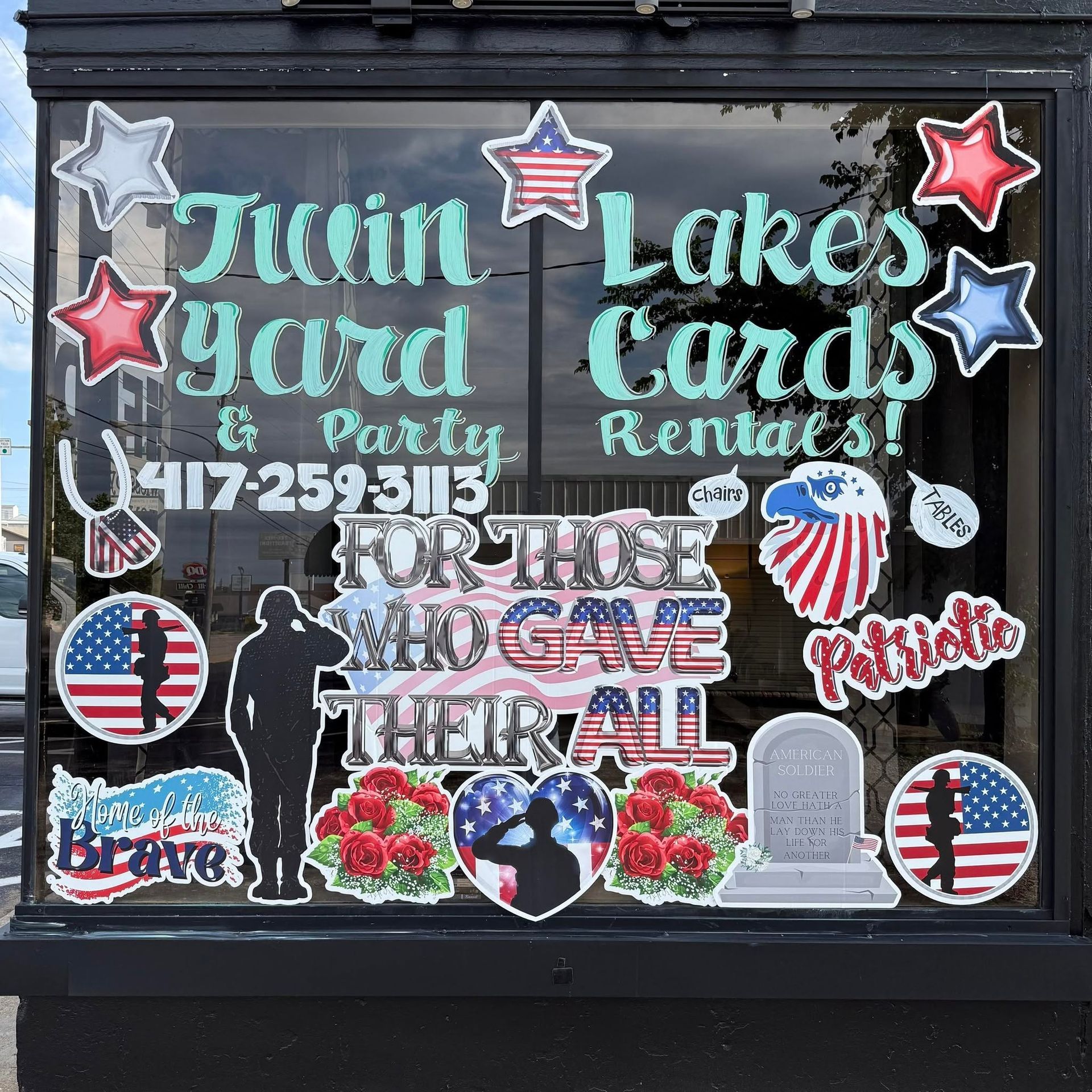Patriotic lawn sign advertising twin yards, card rentals, and a memorial tribute with stars and flowers
