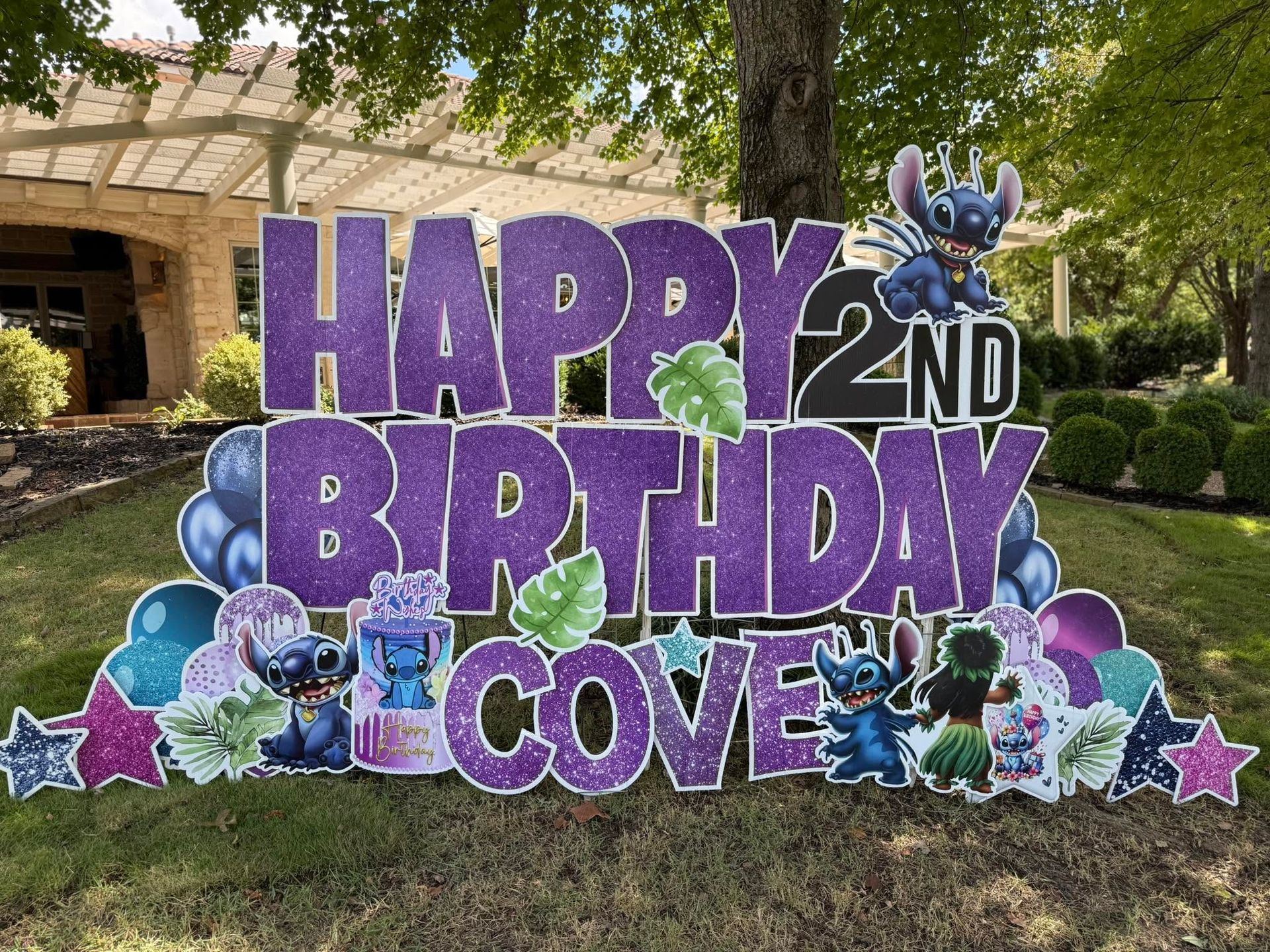 Purple “Happy 2nd Birthday Cove” yard sign with dinosaurs and stars in a grassy outdoor setting