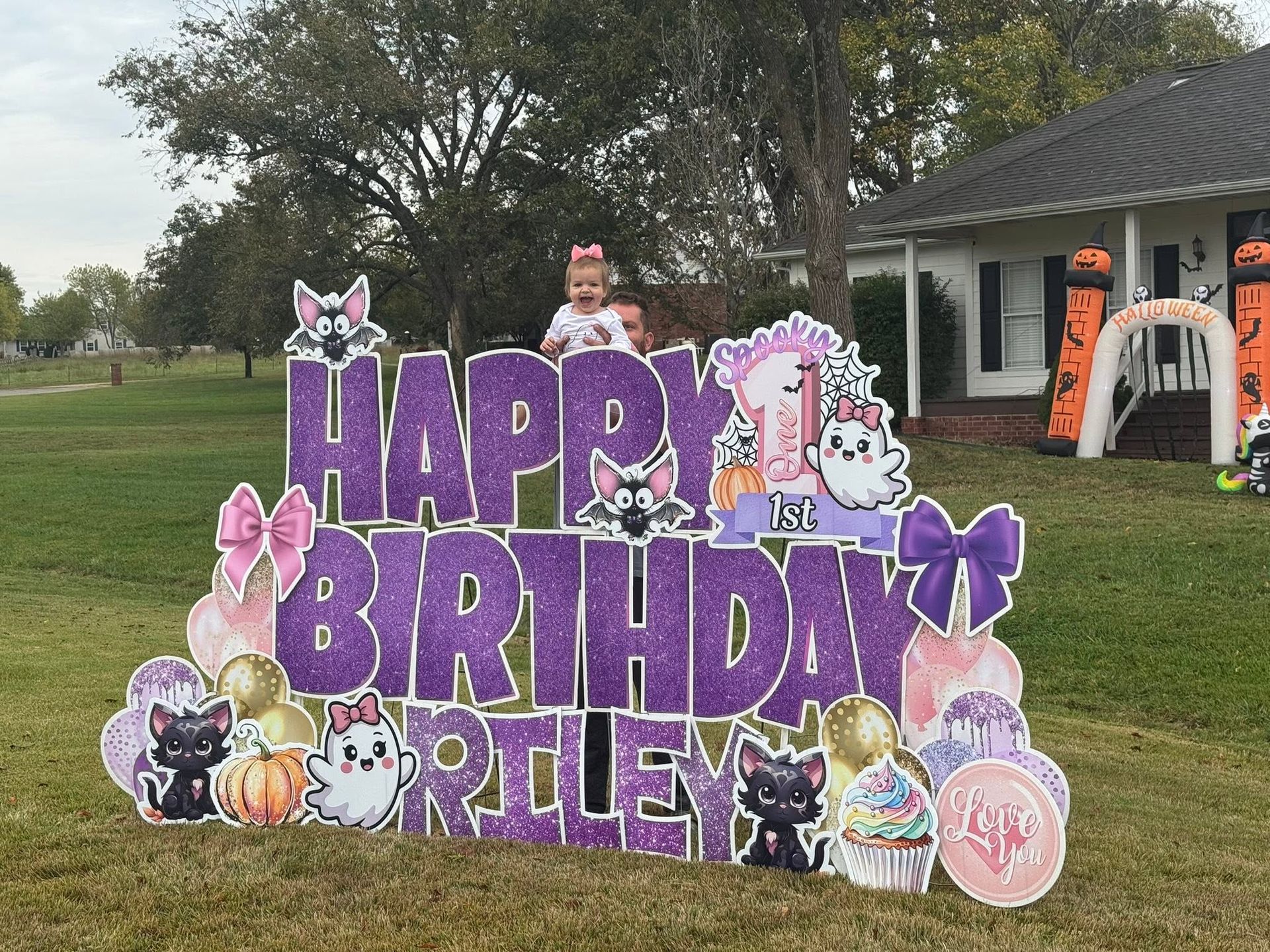 Purple birthday sign on a lawn reading “Happy Birthday,” with bunny cutouts and house in the background